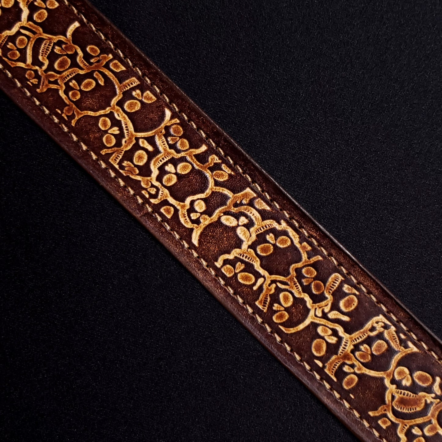 Brown leather belt strap with consistent stitching and a decorative skull pattern.