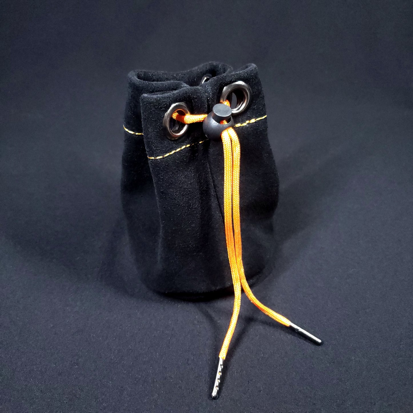 Black suede leather pouch with orange stitching and an orange drawstring, pulled closed.