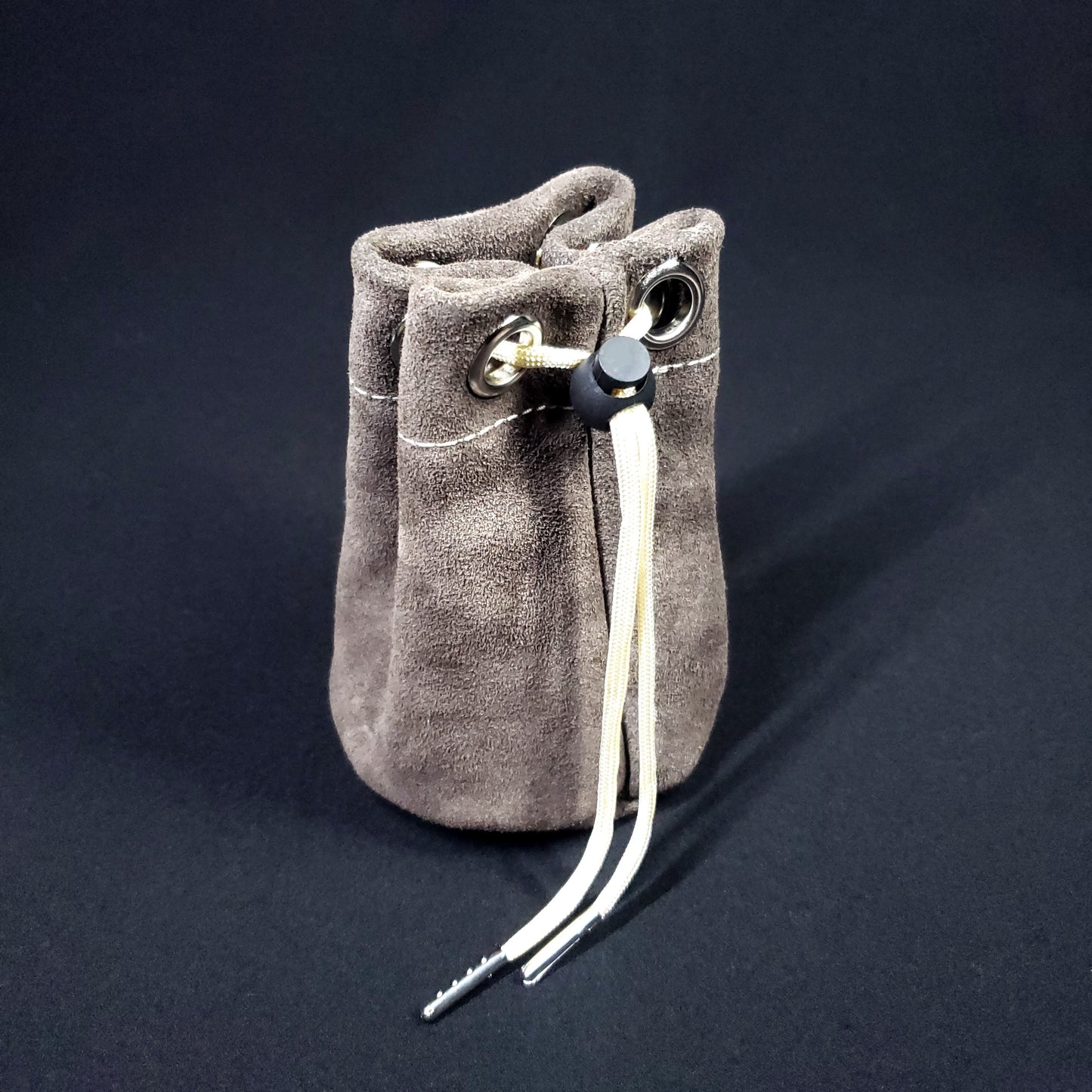 Grey suede leather pouch with champagne colored stitching and a matching drawstring, pulled closed.