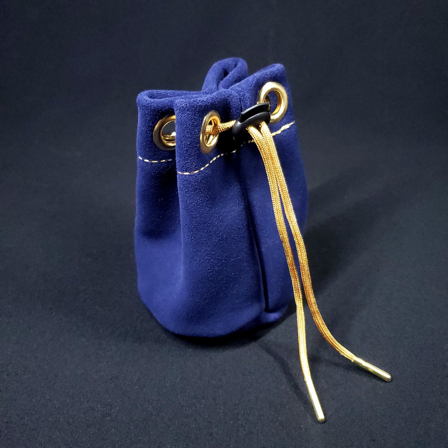 Navy blue suede leather pouch with gold stitching and a gold drawstring, pulled closed.