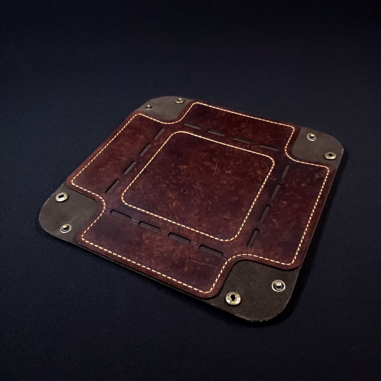 Brown leather dice tray with light brown stitching and bronze buttons, opened and laid flat.