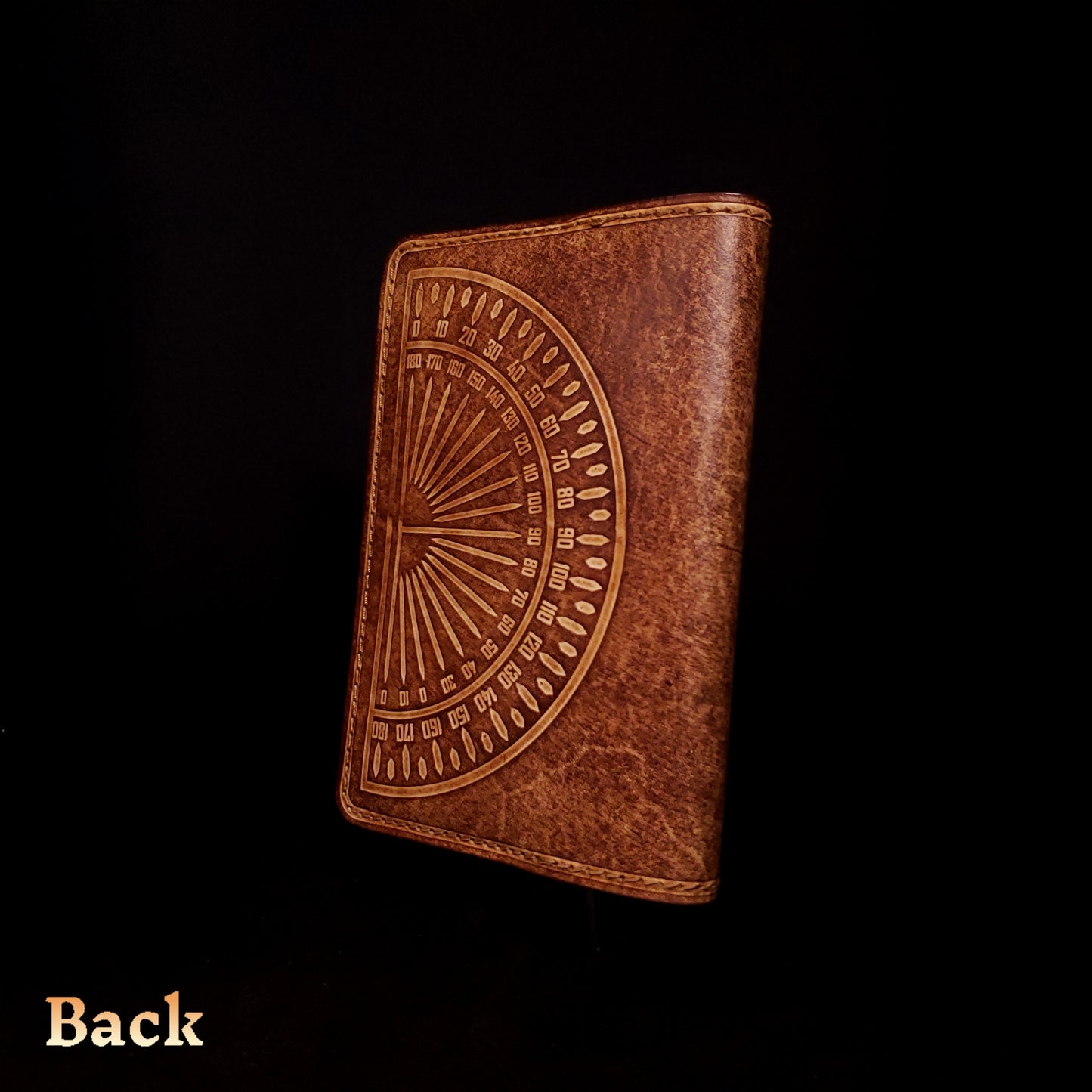 Brown leather notebook cover that's embossed with a protractor design, viewed from the back.