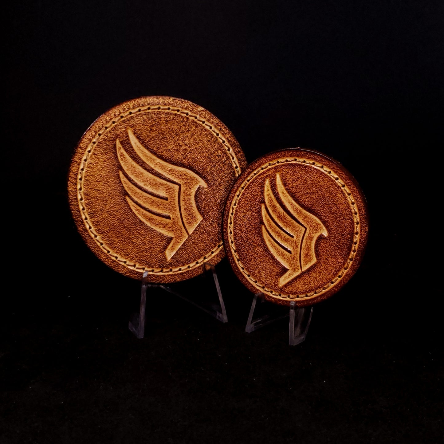Two brown leather velcro patches embossed with a wing symbol from the Mass Effect franchise, posed on a black background.