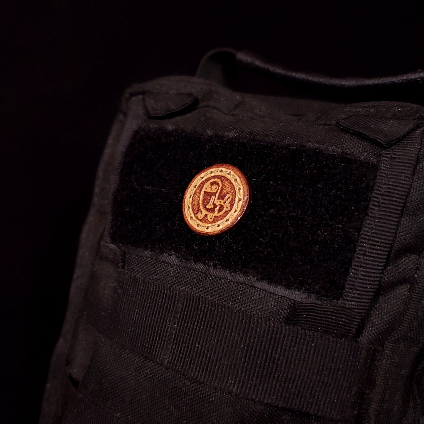Small leather velcro patch embossed with an internet meme character called Dick Butt, affixed to a bag.
