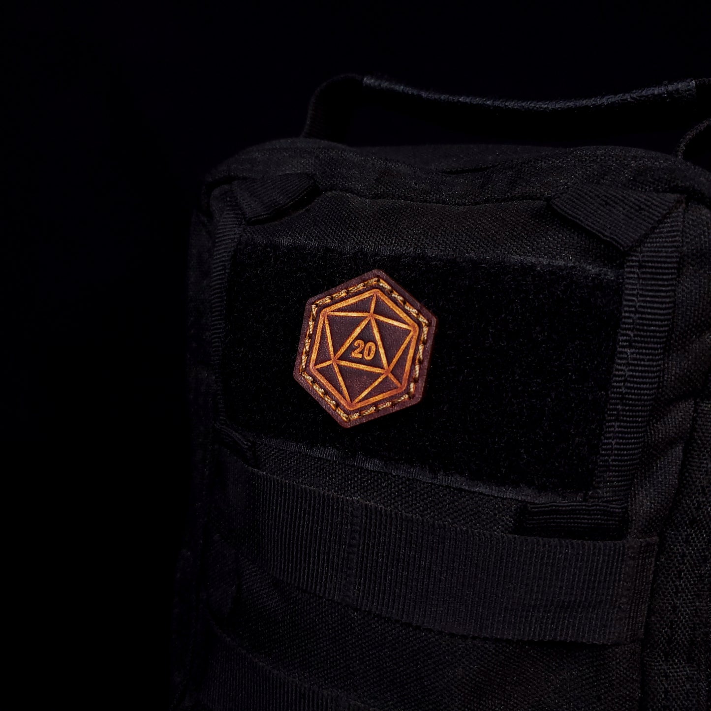 Small leather velcro patch embossed with a twenty-sided die with the number twenty facing up, affixed to a bag.