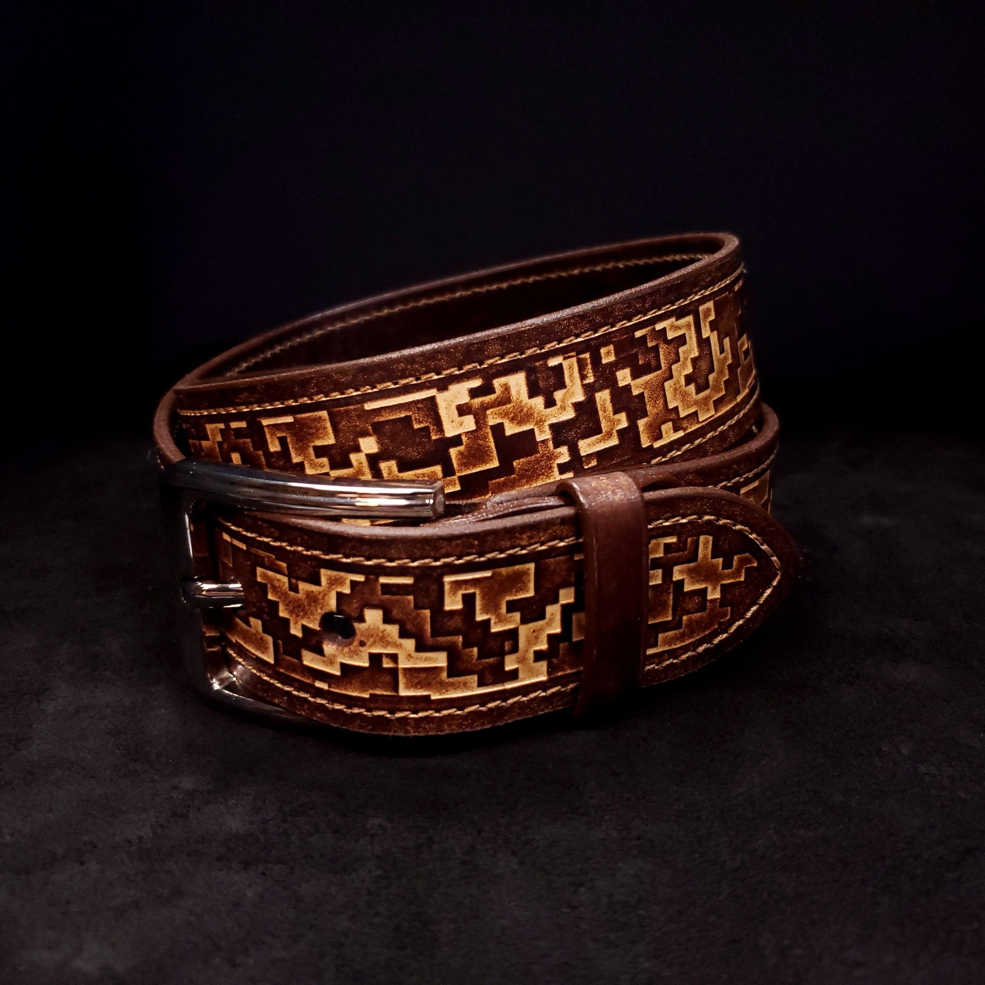 Brown leather belt with a silver buckle, decorated with a digital camouflage pattern and coiled on itself.