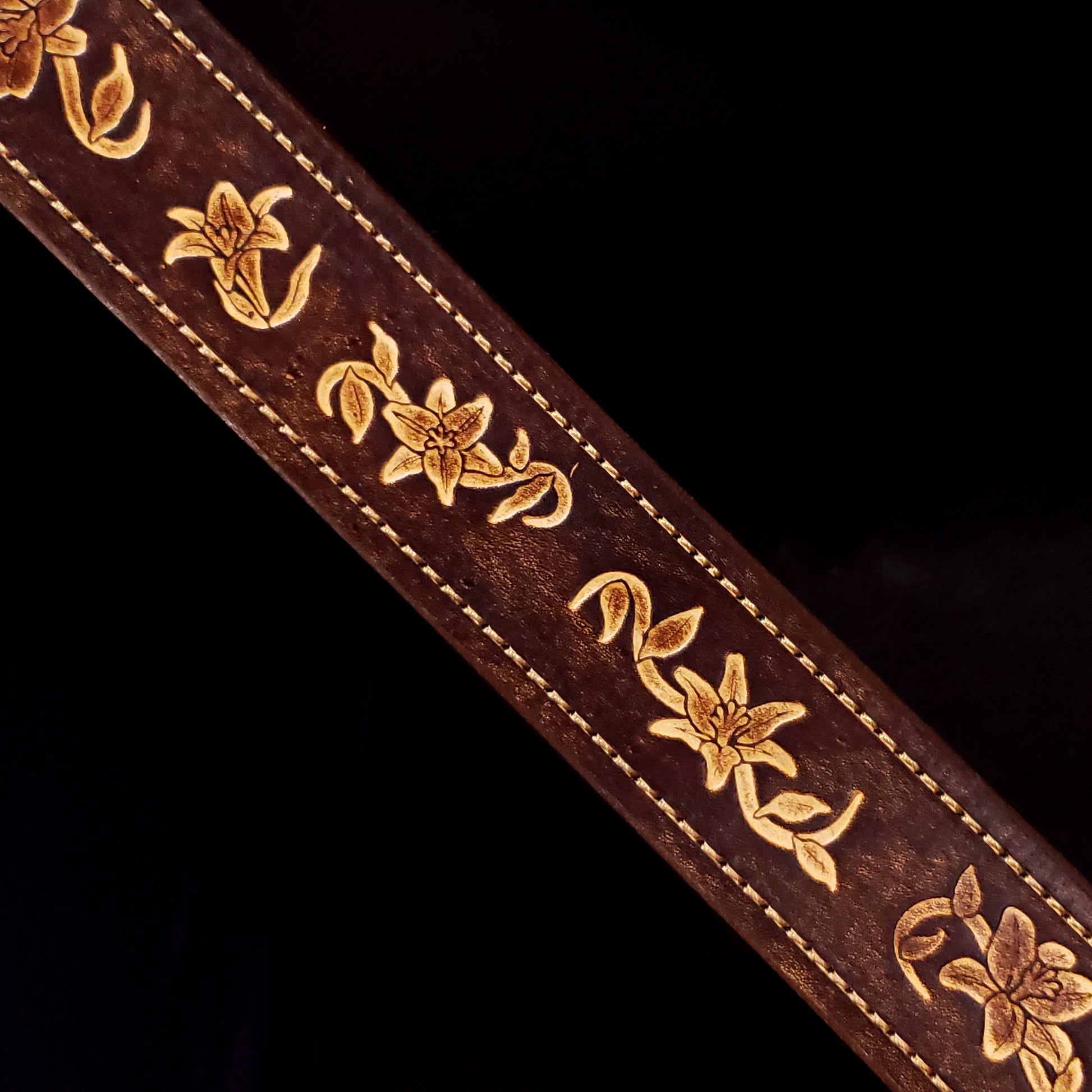 Brown leather belt strap with consistent stitching and floral embossing.