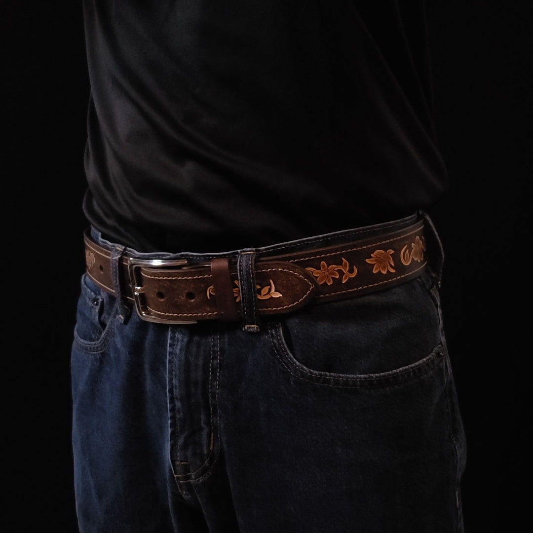 Brown leather belt with a silver buckle and decorated with floral embossing, being worn by a man with jeans.