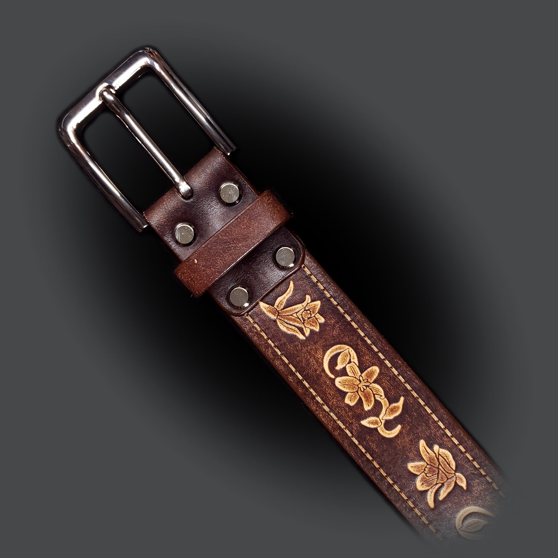 Brown leather belt with a silver buckle, decorated with floral embossing.