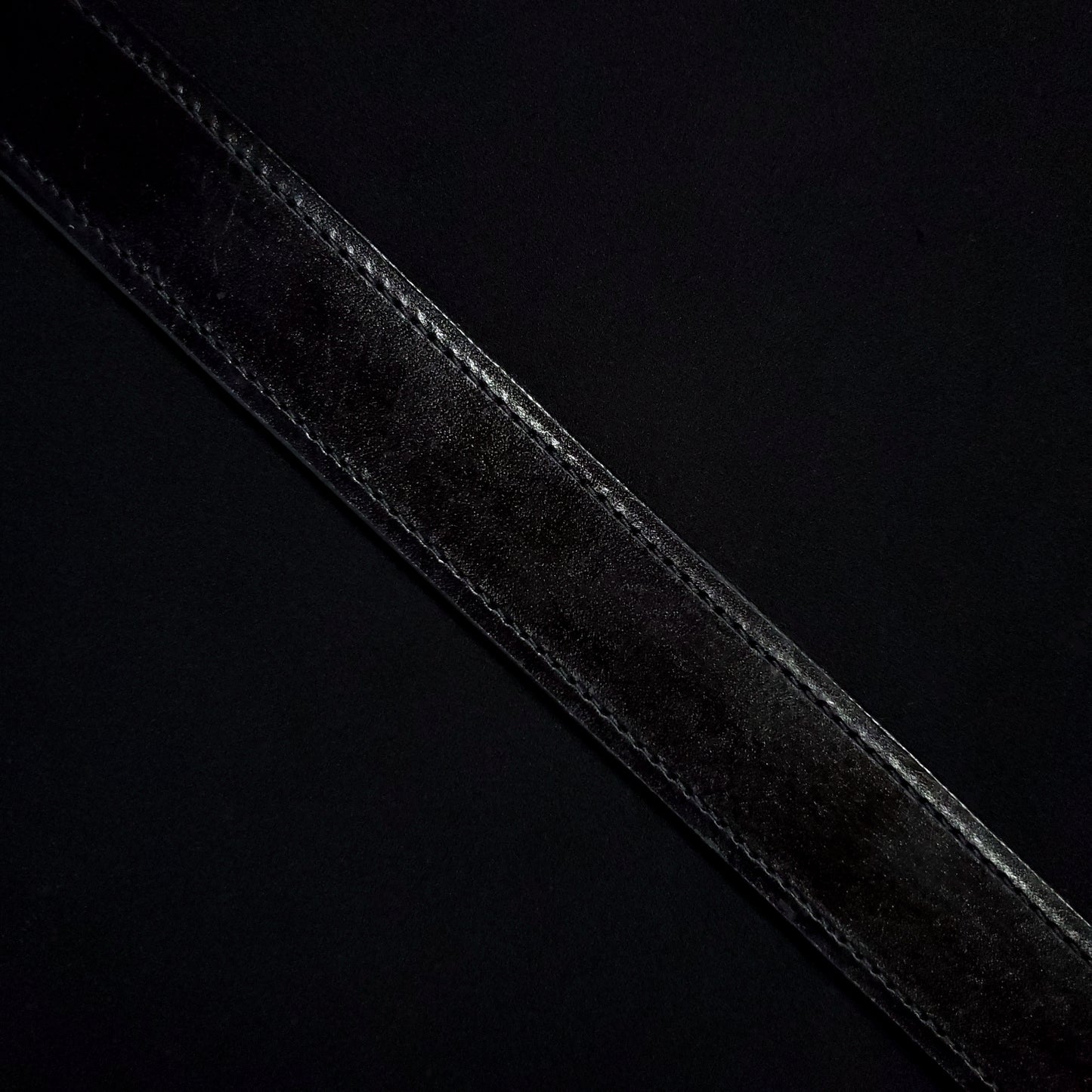 Black leather belt strap with black consistent stitching along either side.