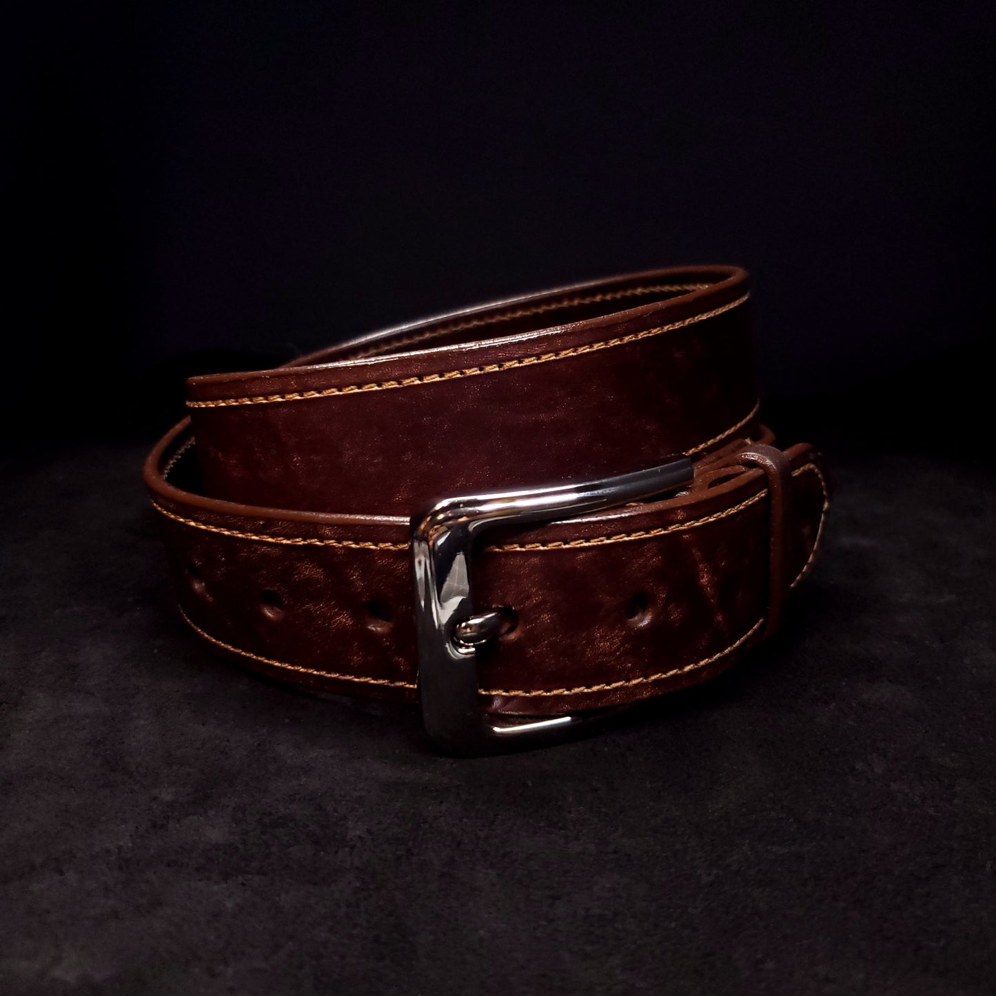 Brown leather belt with light brown stitching and a silver buckle, coiled and fastened to its second notch.