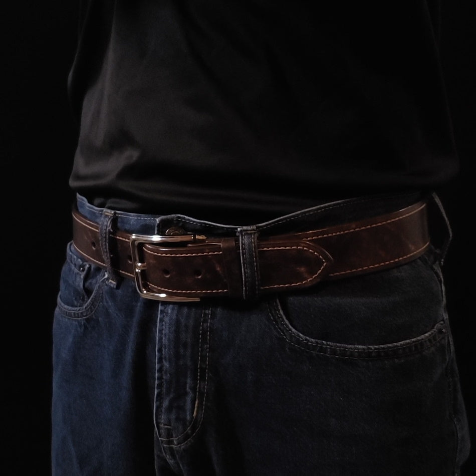 Brown leather belt with light brown stitching and a silver buckle, being worn by a man with jeans.