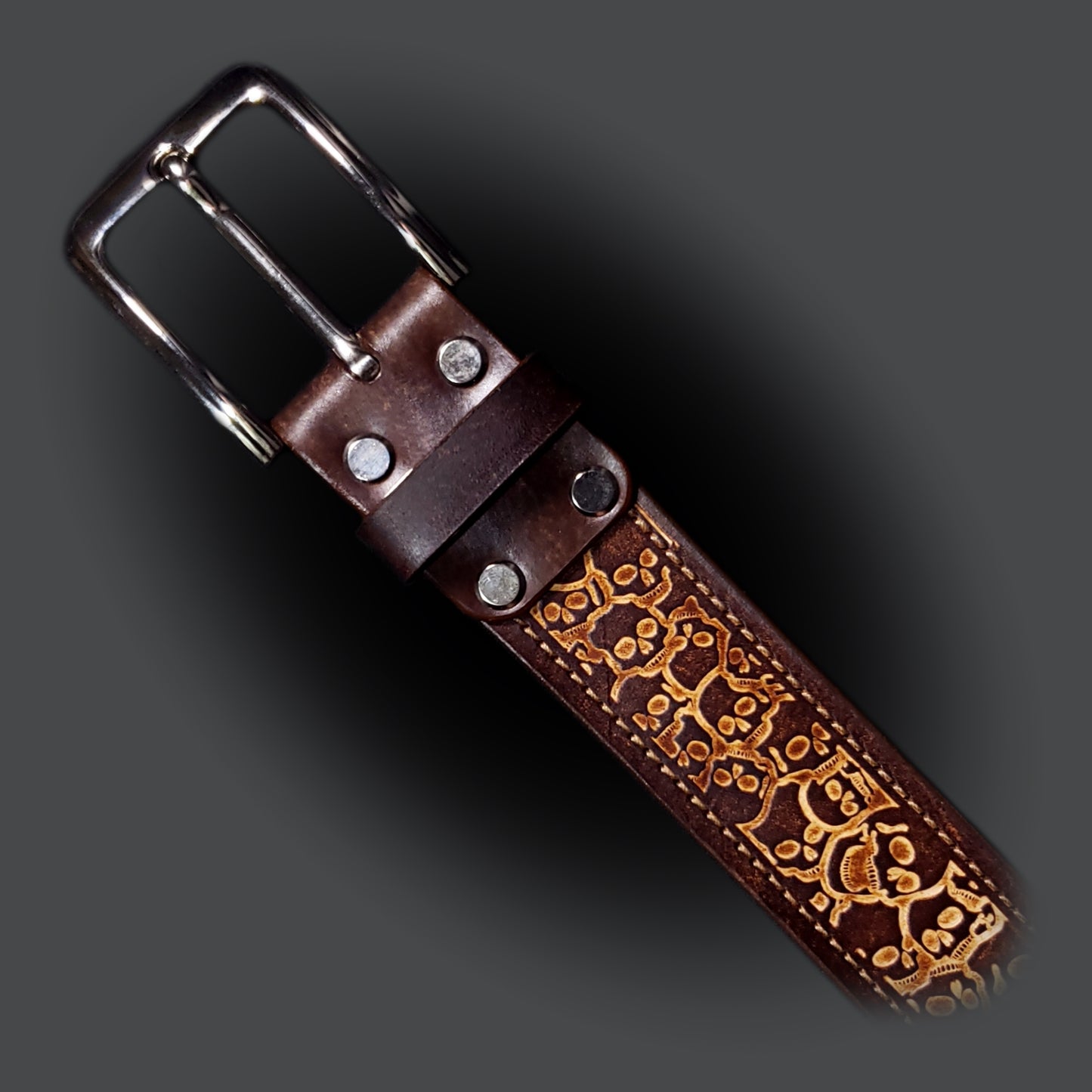 Brown leather belt with a silver buckle, decorated with a skull pattern.