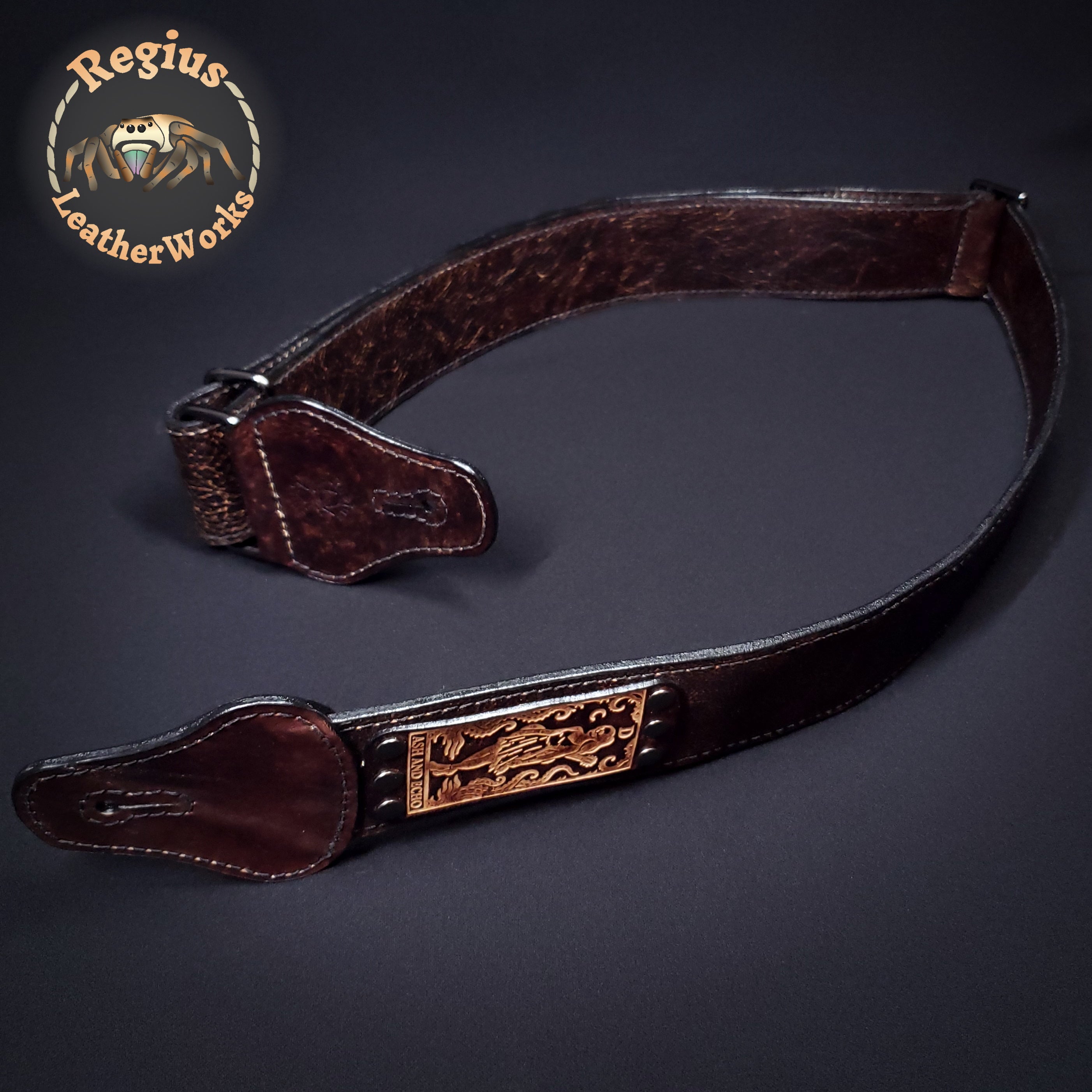 Brown leather guitar strap with decorative embossed plate on a dark background