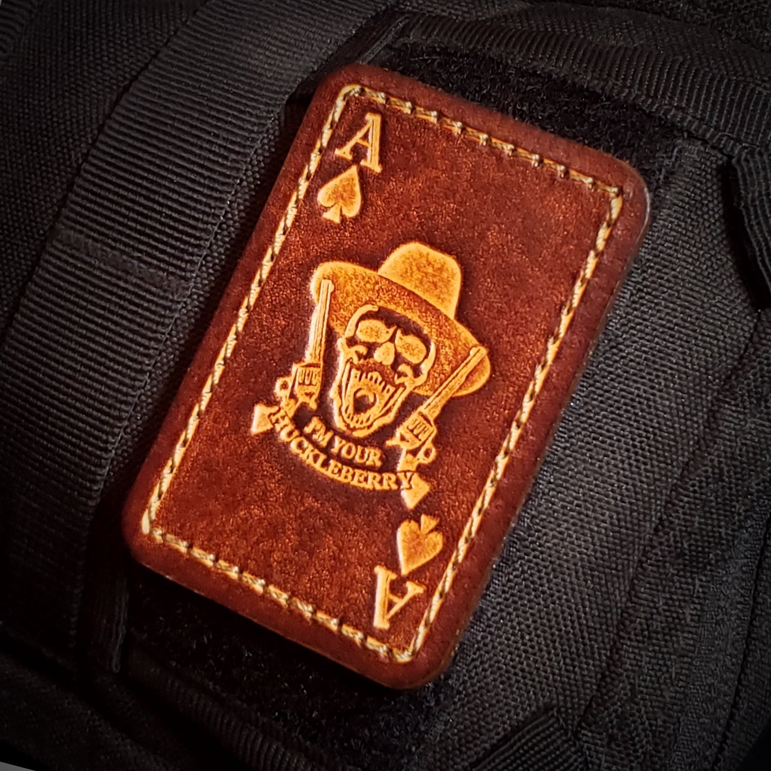 Brown leather patch with an ace of spades design featuring a skull, guns, and text saying "I'm your huckleberry"