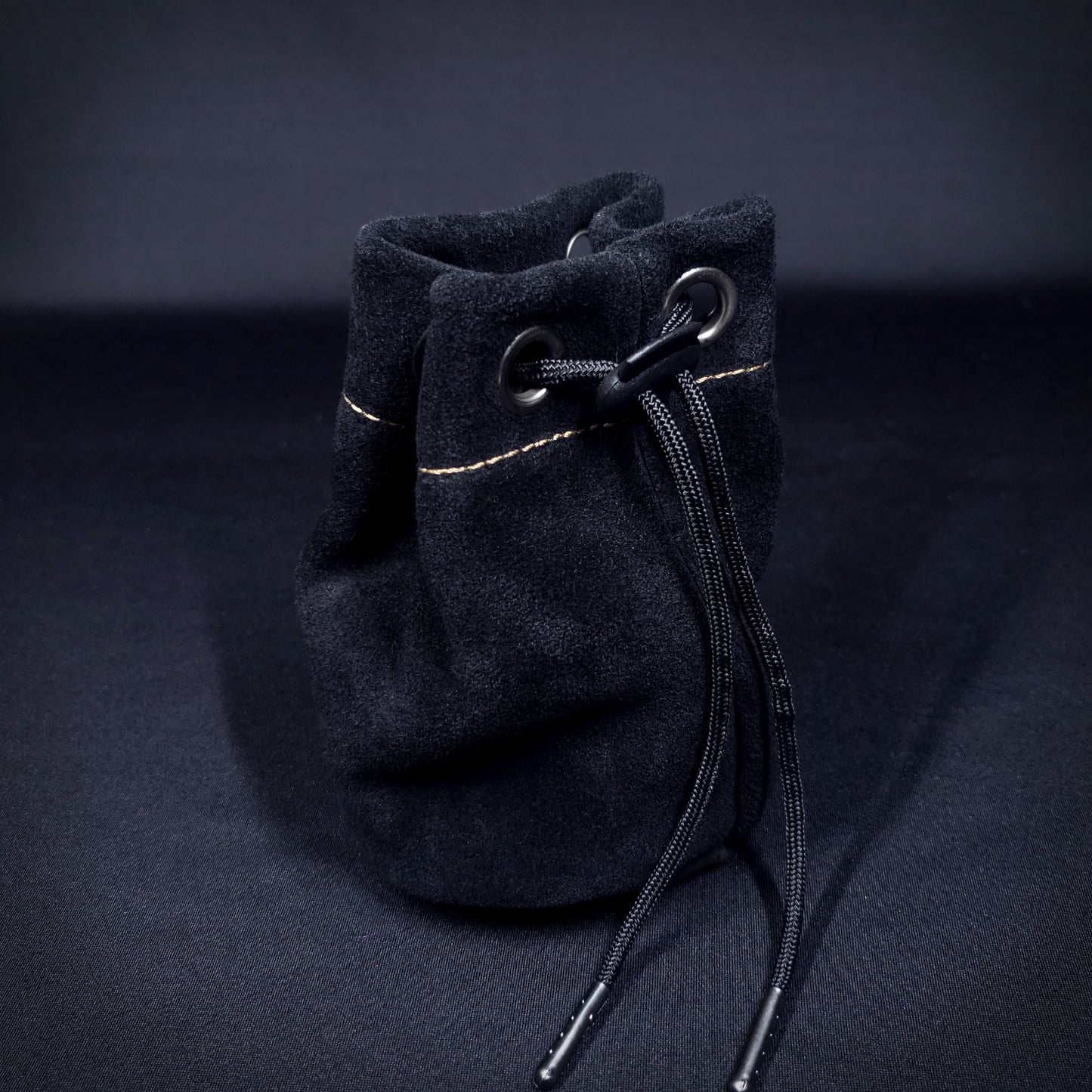 Black suede leather pouch with brown stitching and a black drawstring, pulled closed.