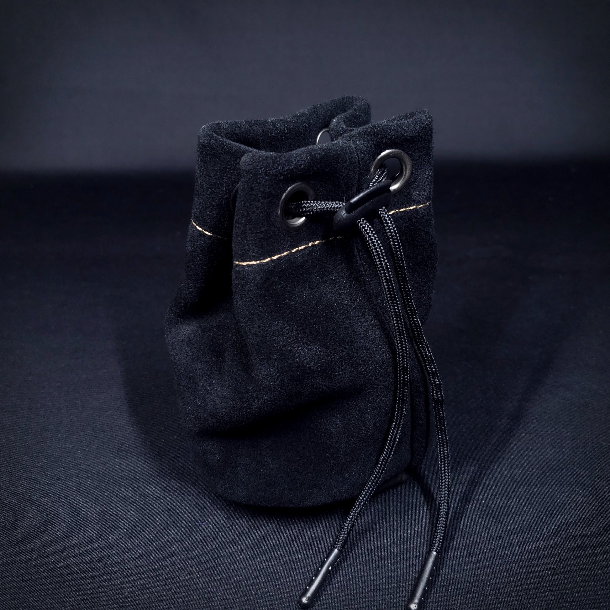 Black suede leather pouch with brown stitching and a black drawstring, pulled closed.