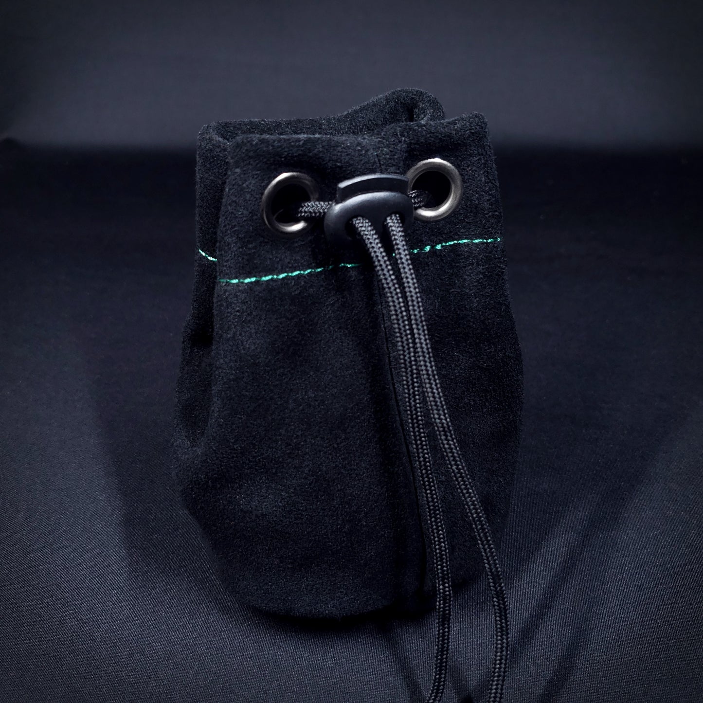 Black suede leather pouch with green stitching and a black drawstring, pulled closed.