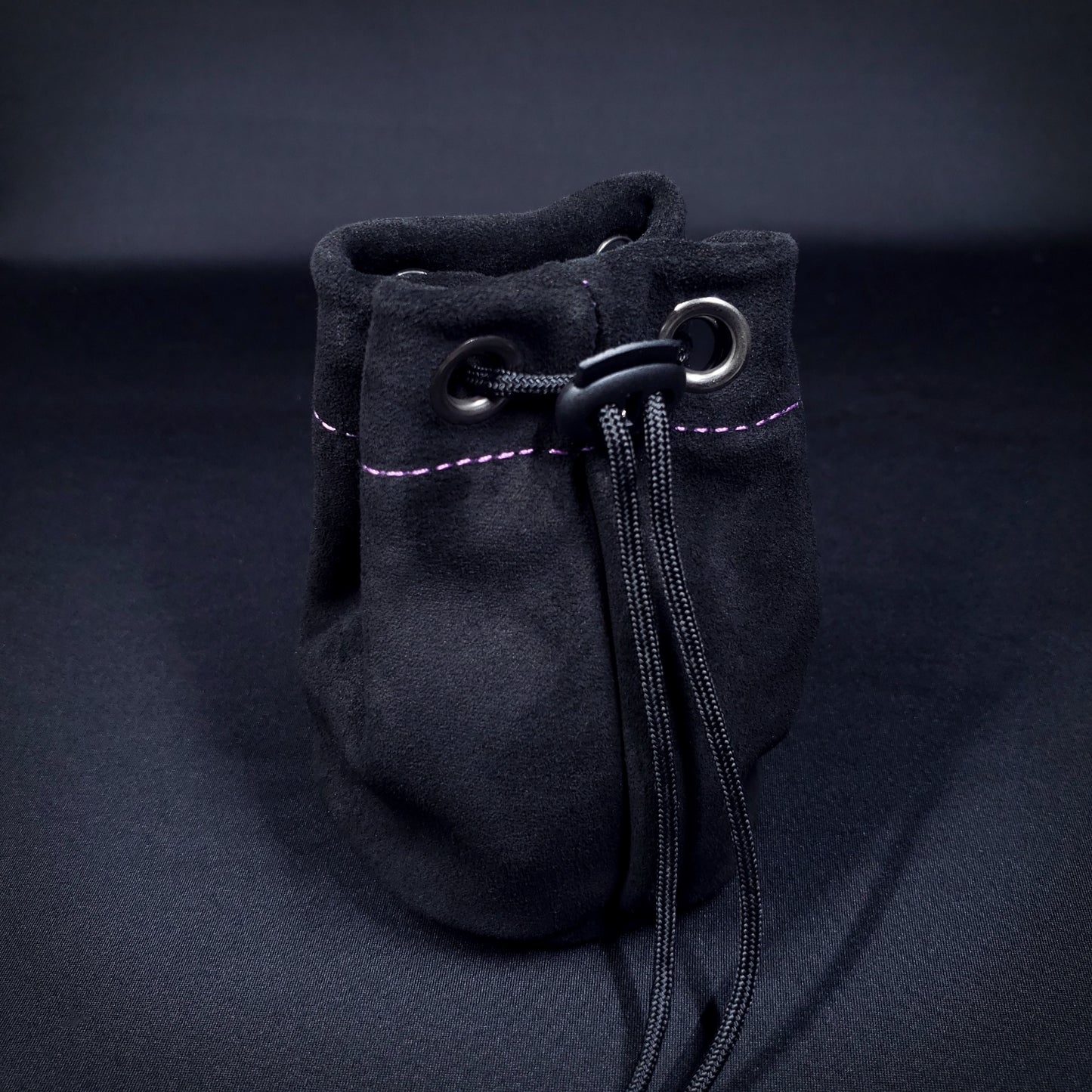 Black suede leather pouch with purple stitching and a black drawstring, pulled closed.