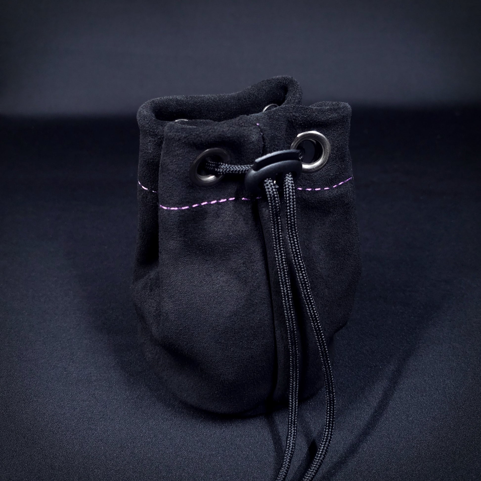 Black suede leather pouch with purple stitching and a black drawstring, pulled closed.