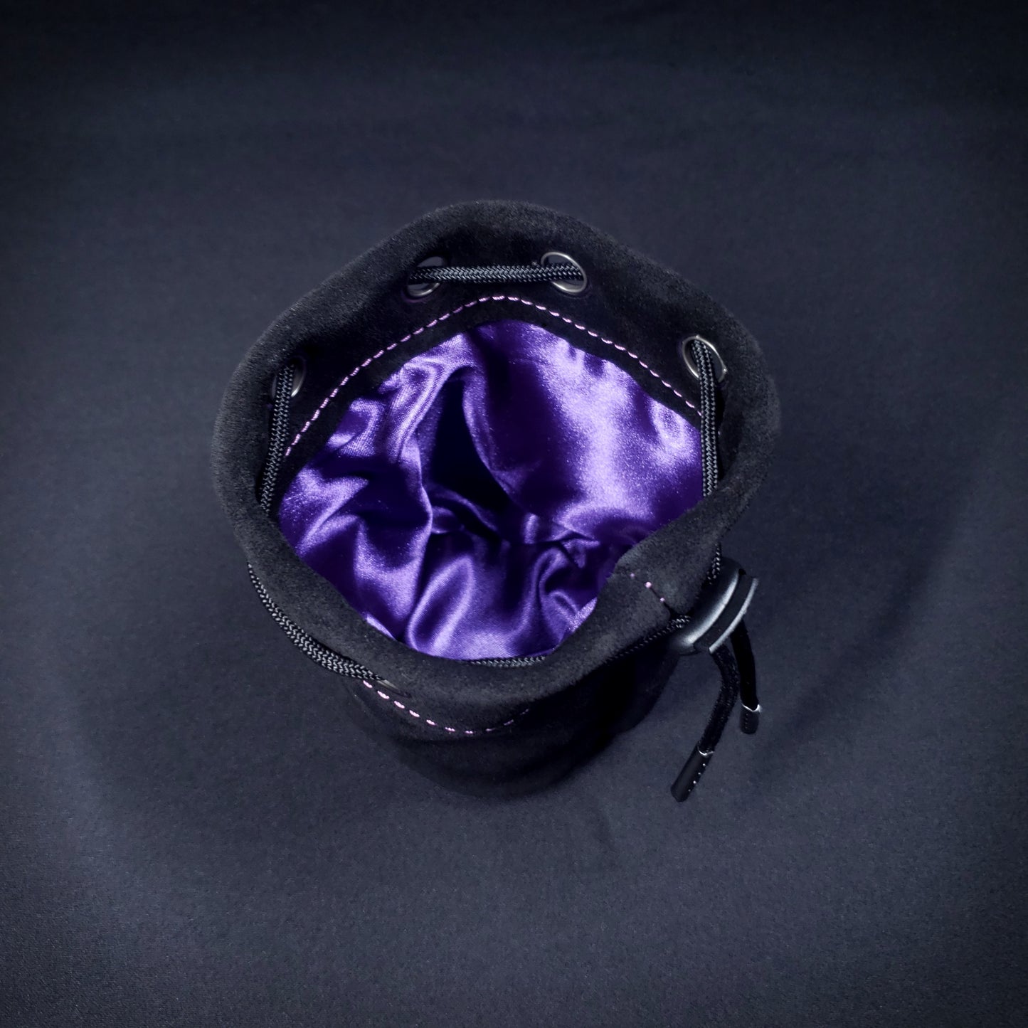 Black suede leather pouch with a black drawstring, looking down into its purple satin interior.