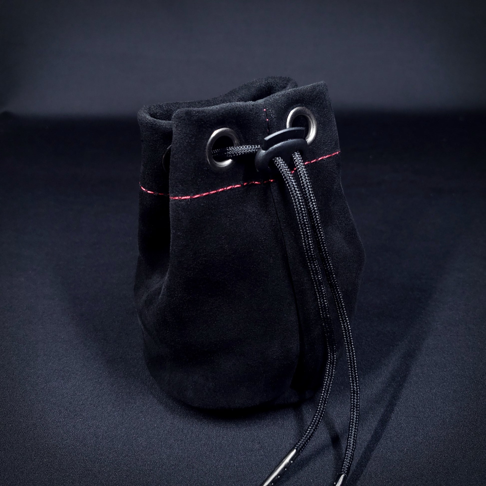 Black suede leather pouch with red stitching and a black drawstring, pulled closed.