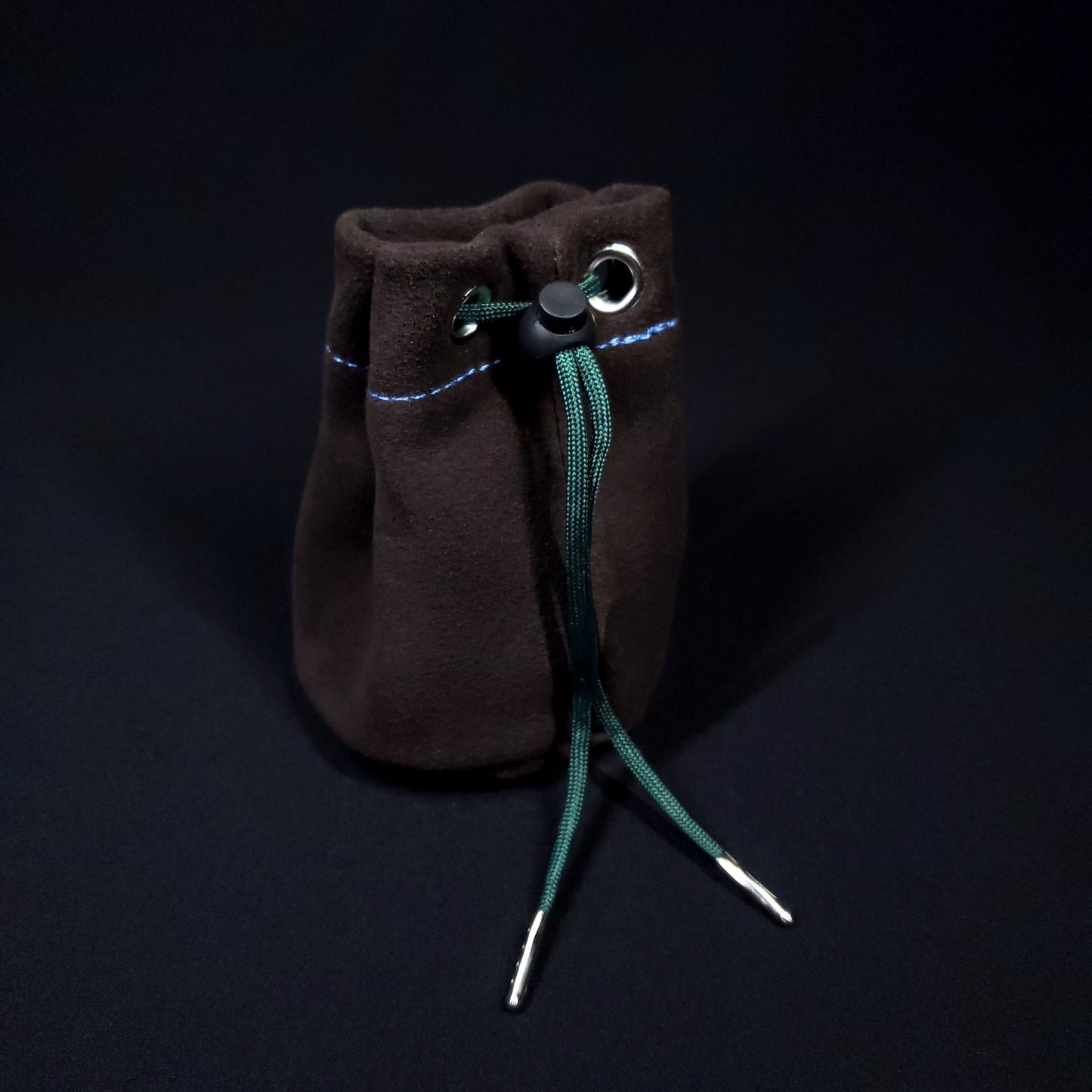 Brown suede leather pouch with a blue and green plaid cloth interior and green drawstring, pulled closed.