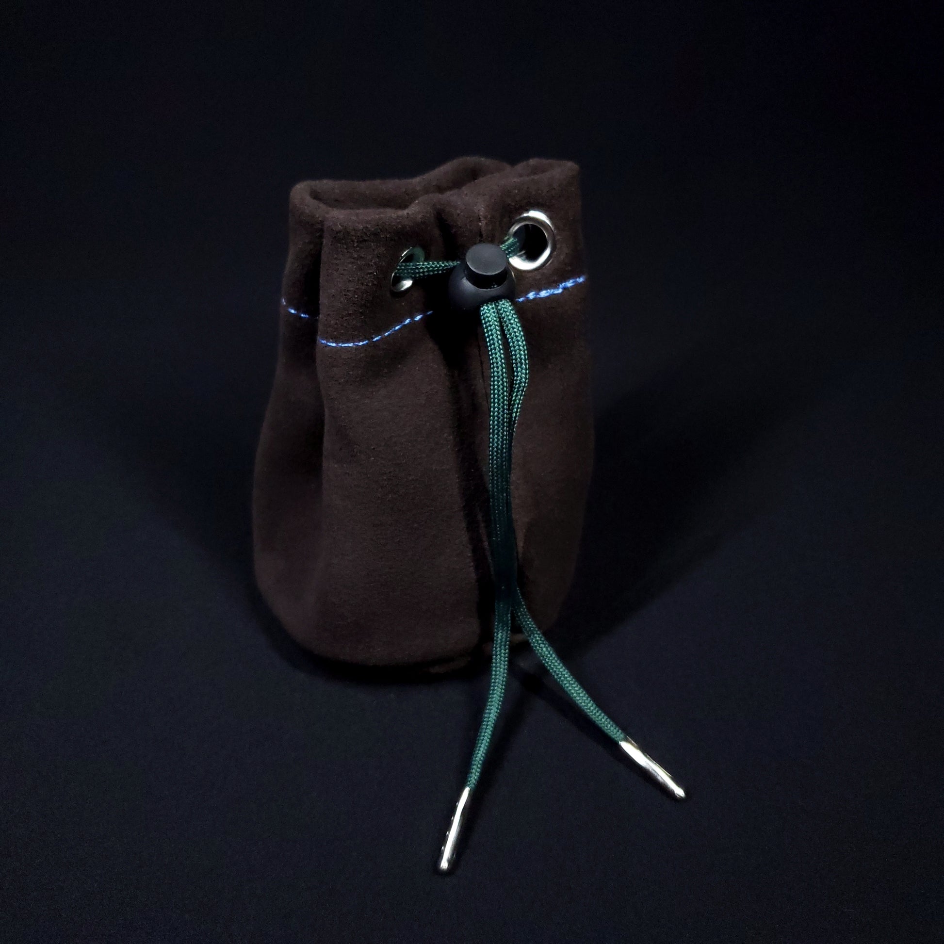 Brown suede leather pouch with a blue and green plaid cloth interior and green drawstring, pulled closed.