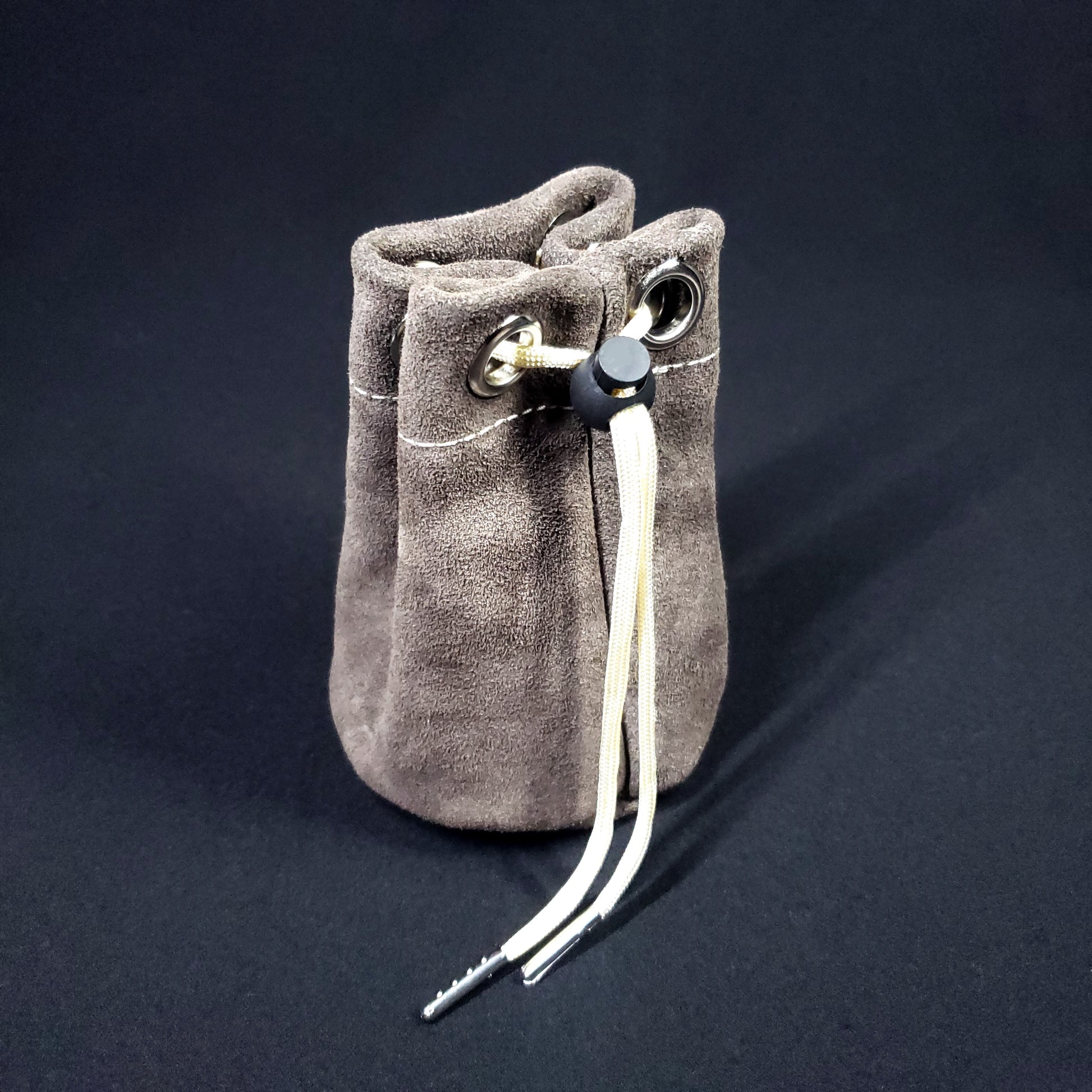 Grey suede leather pouch with champagne colored stitching and a matching drawstring, pulled closed.
