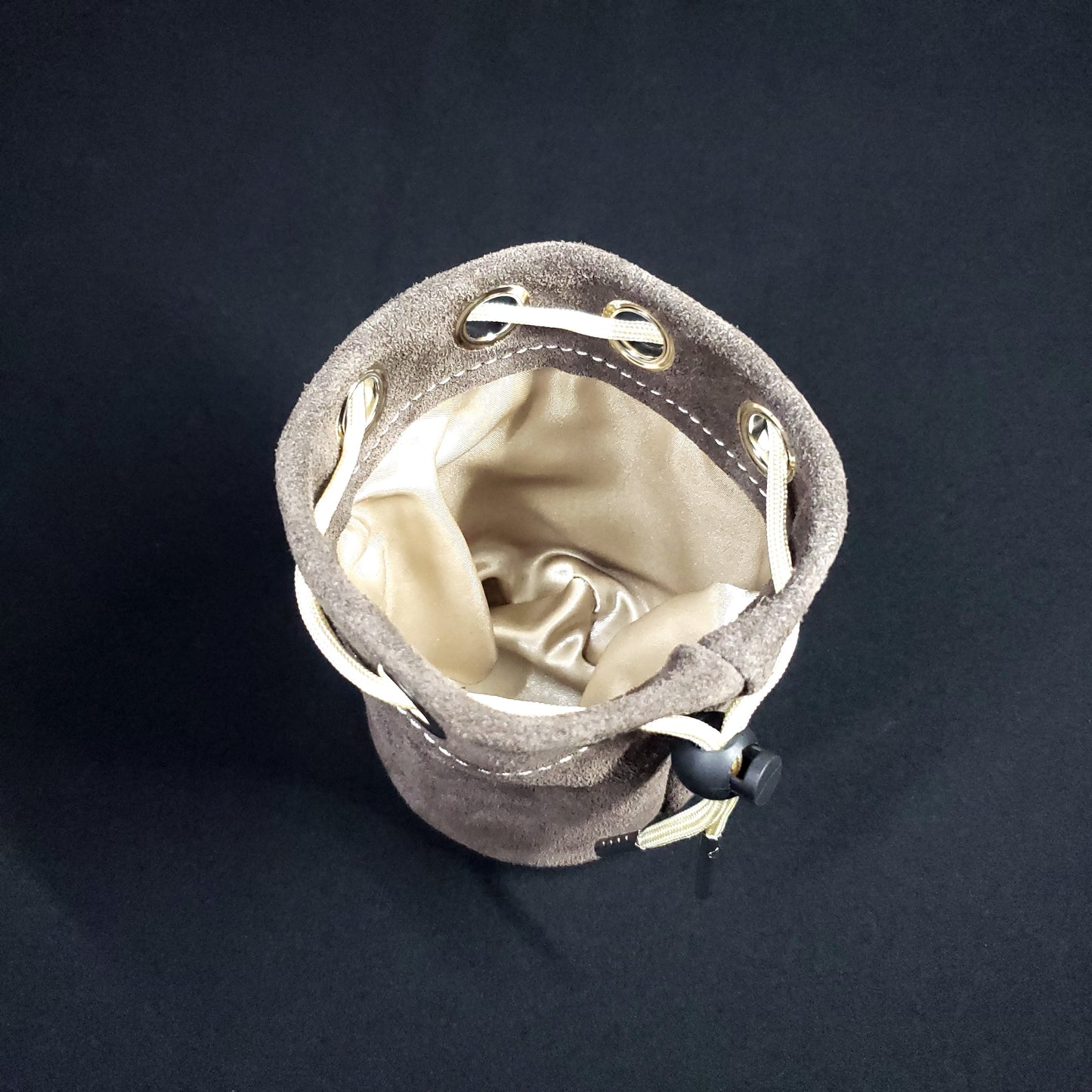 Grey suede leather pouch with a champagne colored drawstring, looking down into its champagne satin interior.