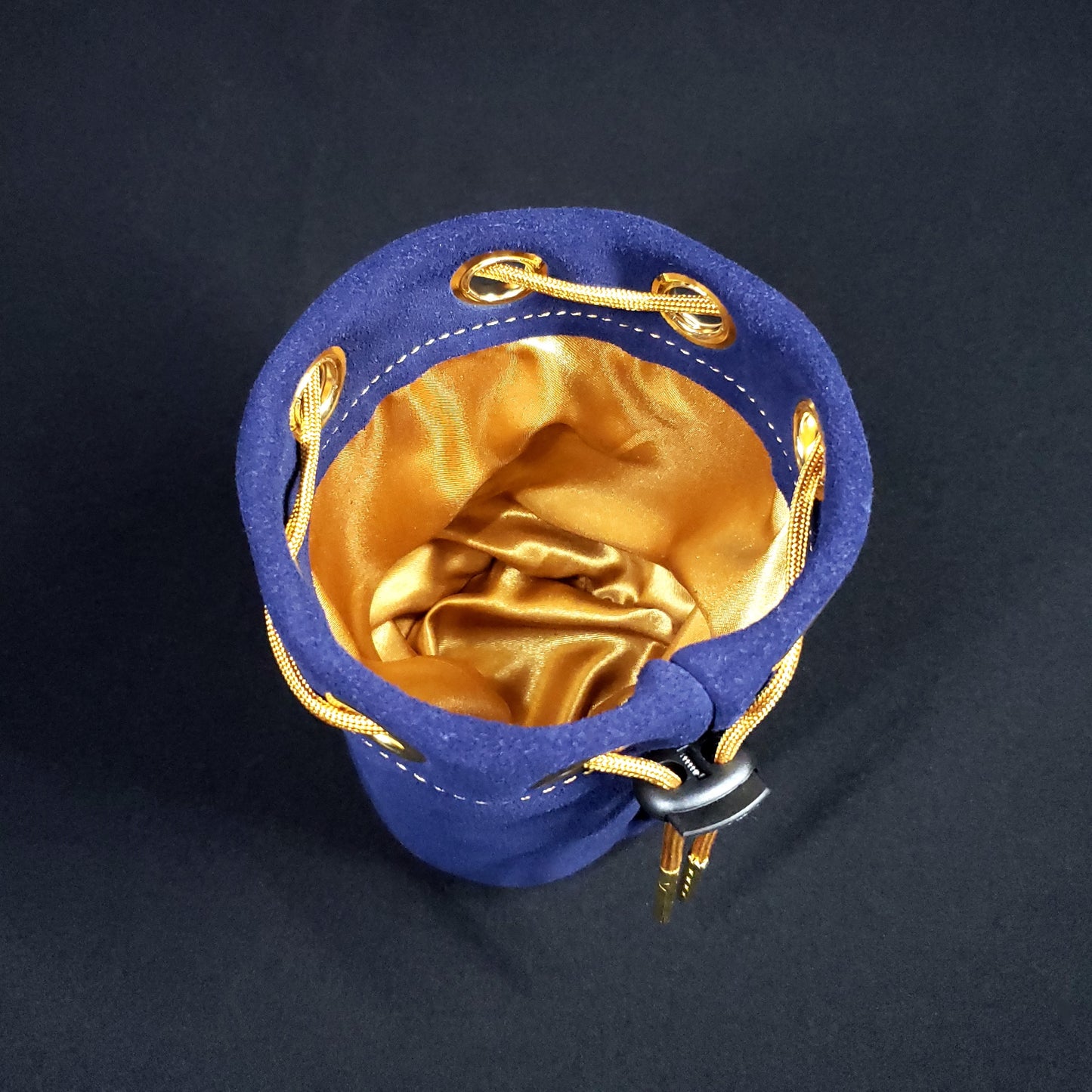 Navy blue suede leather pouch with a gold drawstring, looking down into its gold satin interior.
