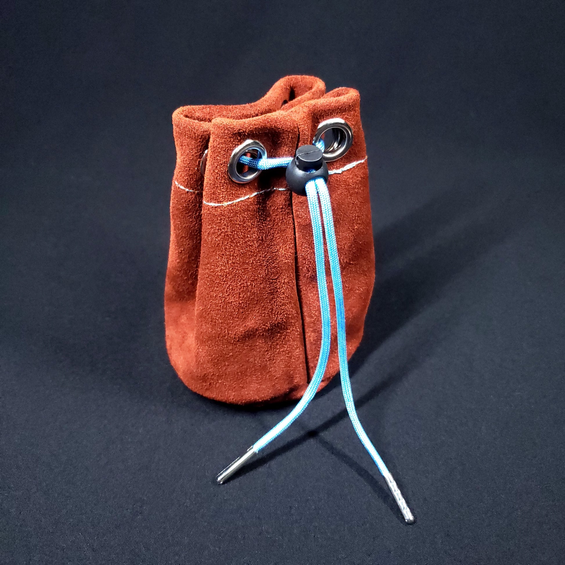 Rust colored suede leather pouch with light blue stitching and a light blue drawstring, pulled closed.