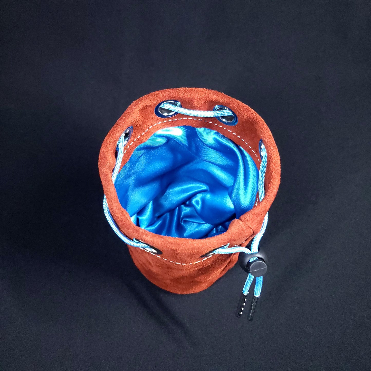 Rust colored suede leather pouch with a light blue drawstring, looking down into its light blue satin interior.