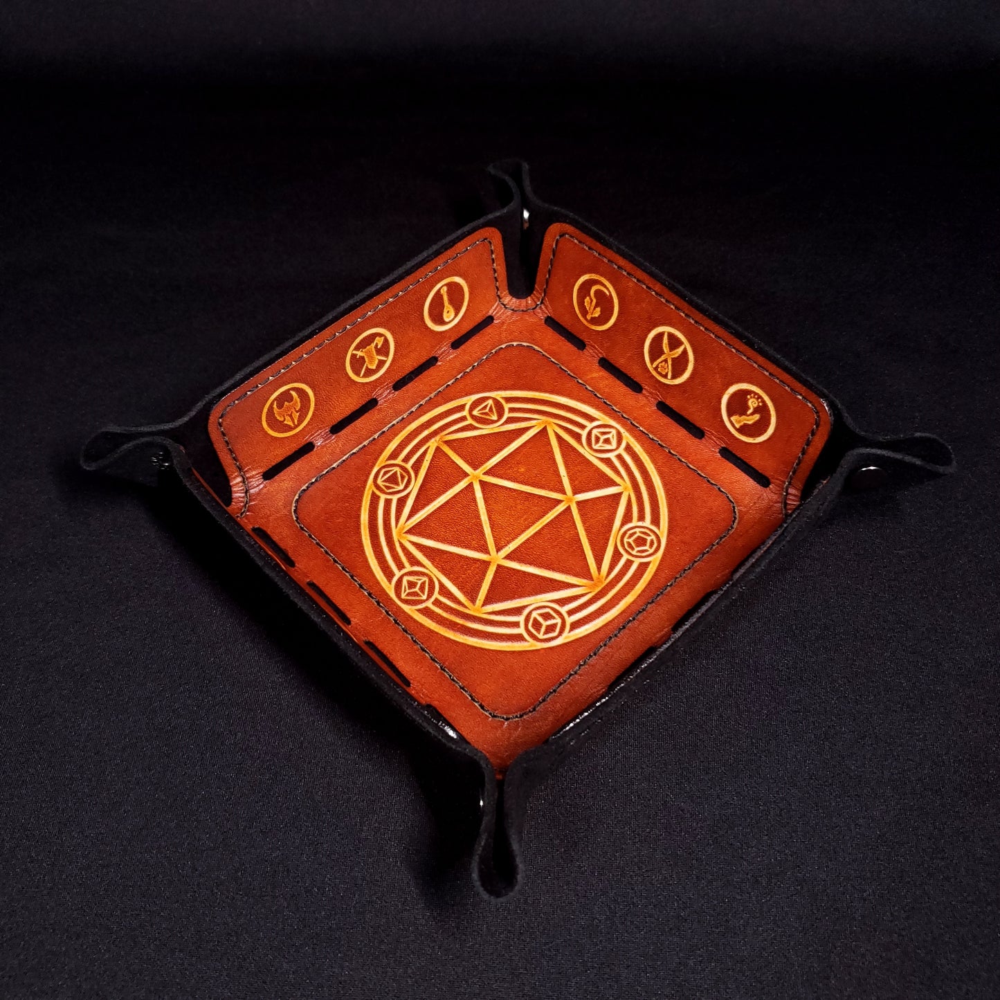 Black and brown leather dice tray decorated with dungeons and dragons icons, viewed from the top.