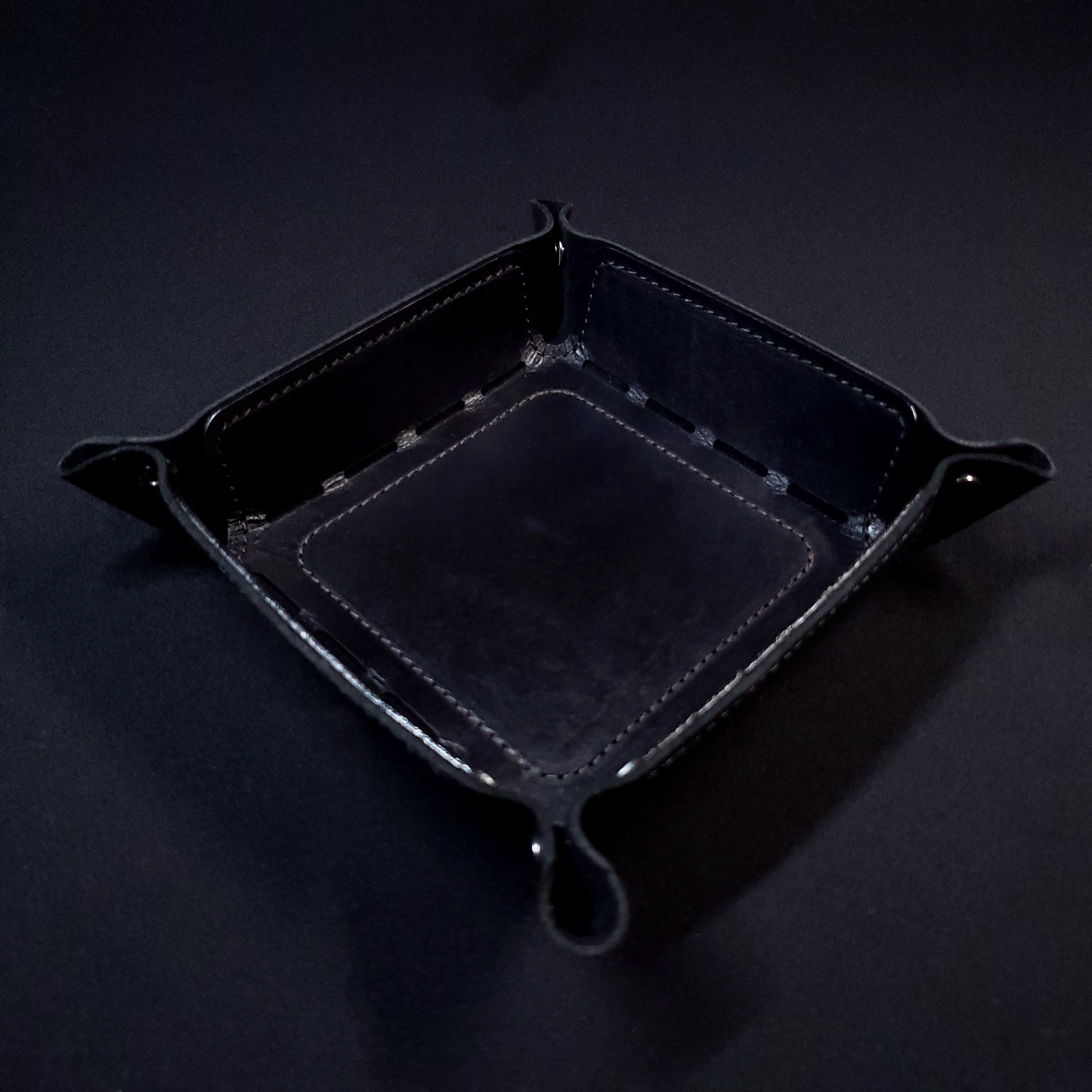 Black leather dice tray with black stitching and gun metal buttons, viewed from the top.