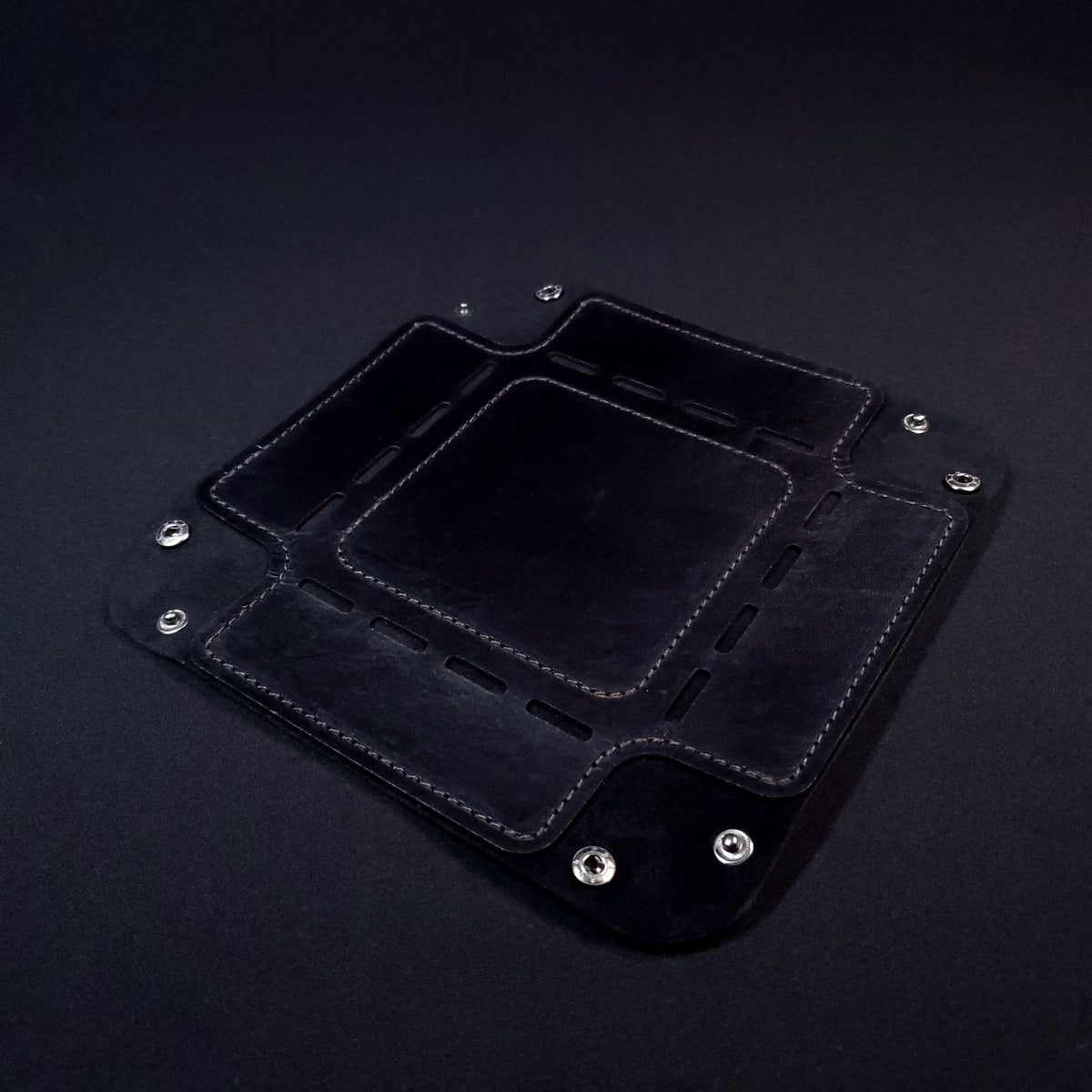 Black leather dice tray with black stitching and gun metal buttons, opened and laid flat.