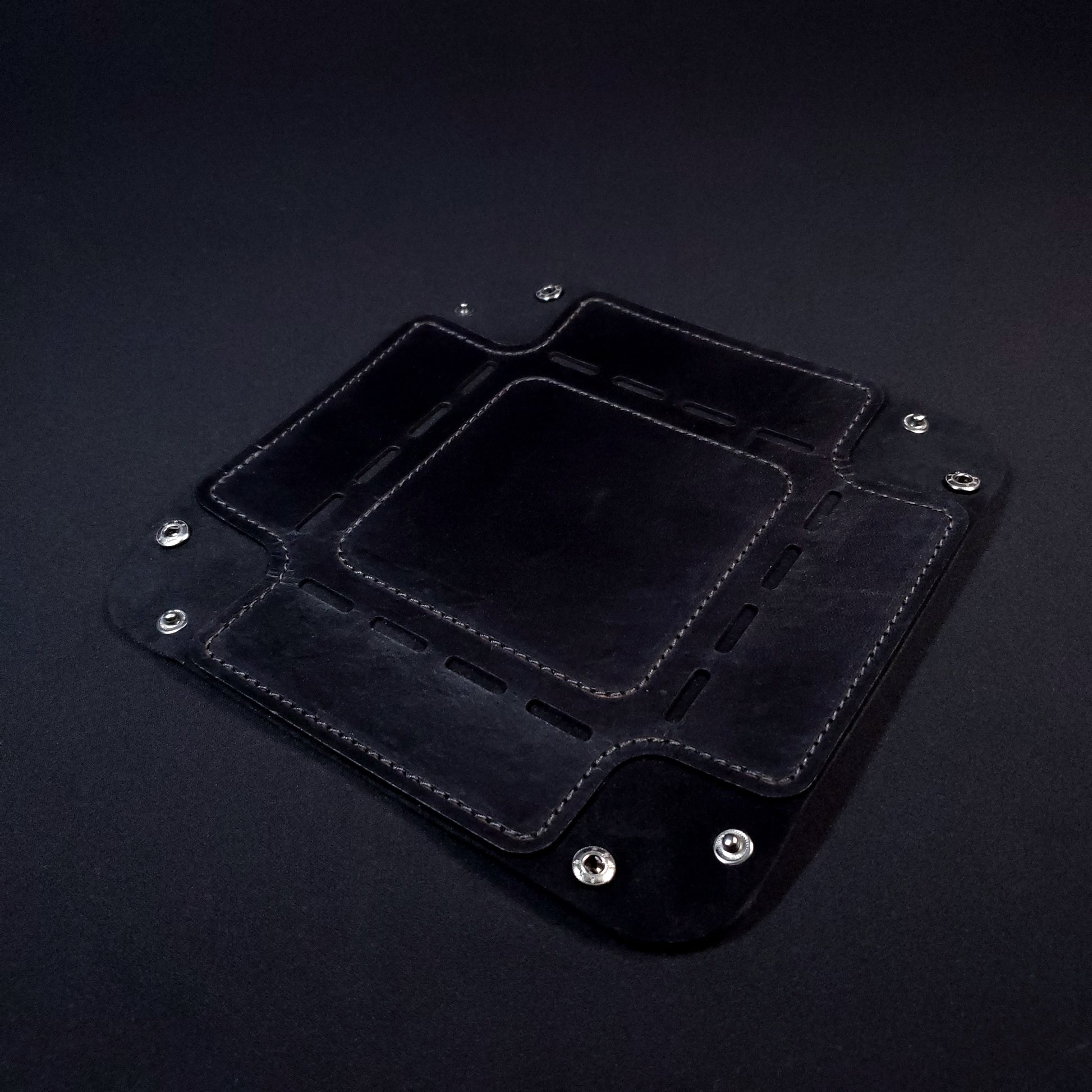 Black leather dice tray with black stitching and gun metal buttons, opened and laid flat.