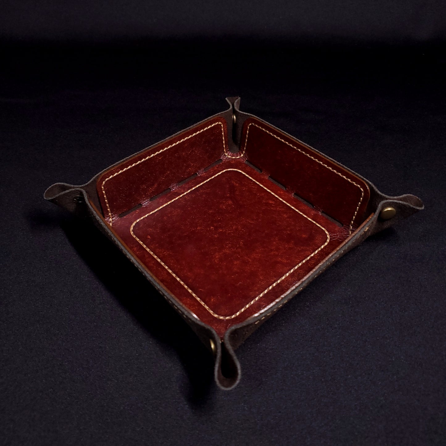 Brown leather dice tray with light brown stitching and bronze buttons, viewed from the top.