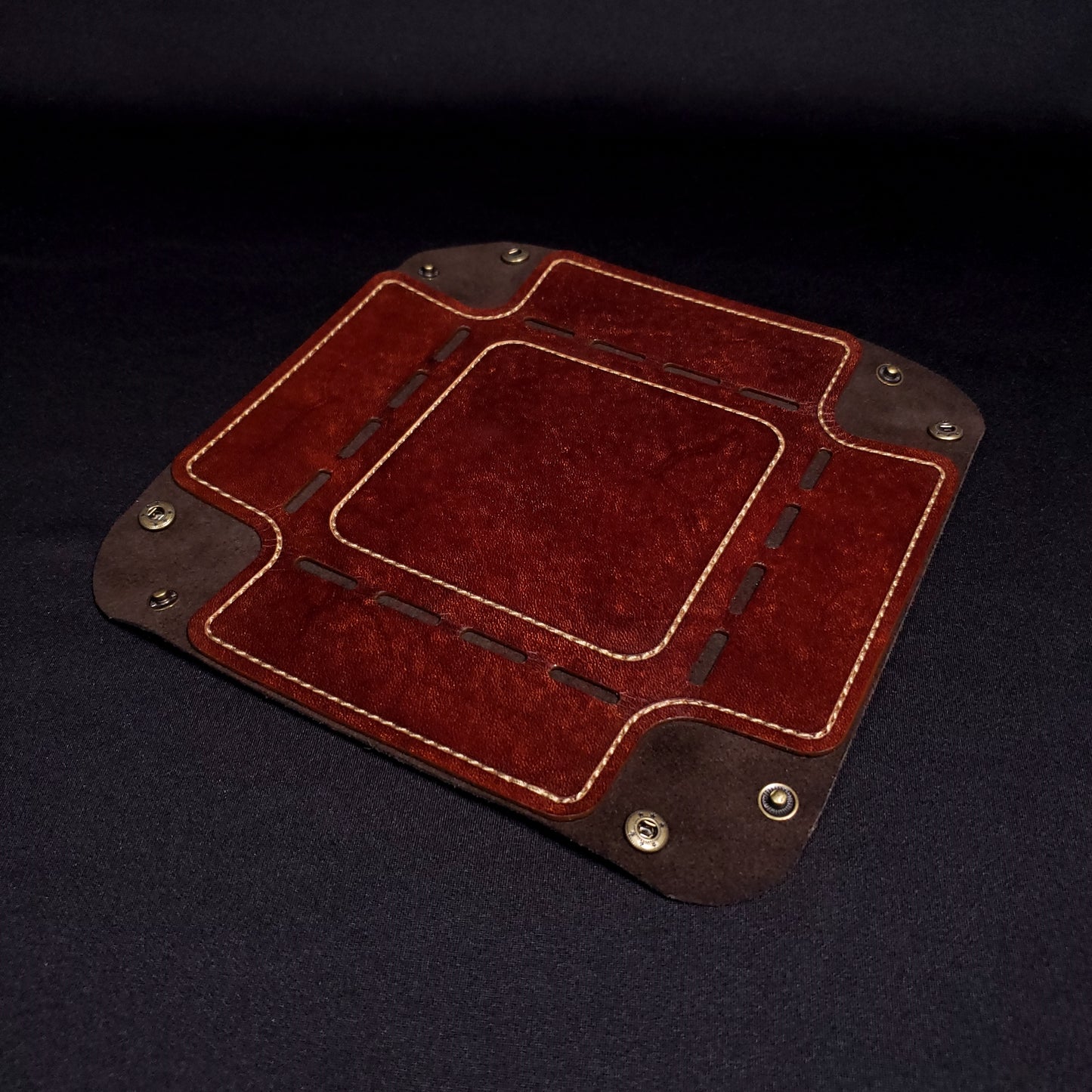 Brown leather dice tray with light brown stitching and bronze buttons, opened and laid flat.