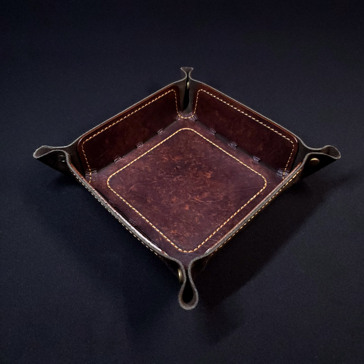 Brown leather dice tray with light brown stitching and bronze buttons, viewed from the top.