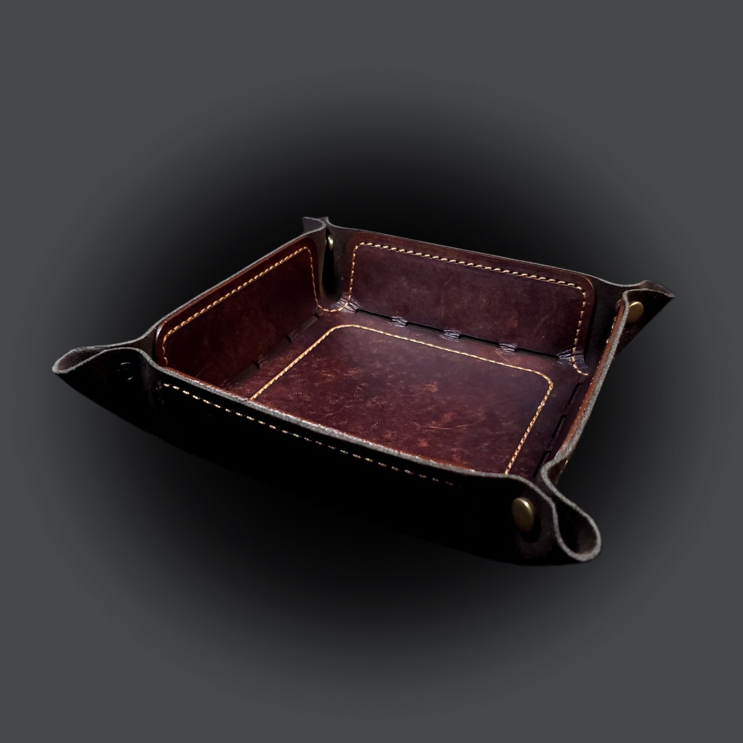Brown leather dice tray with light brown stitching and bronze buttons, viewed from the front.