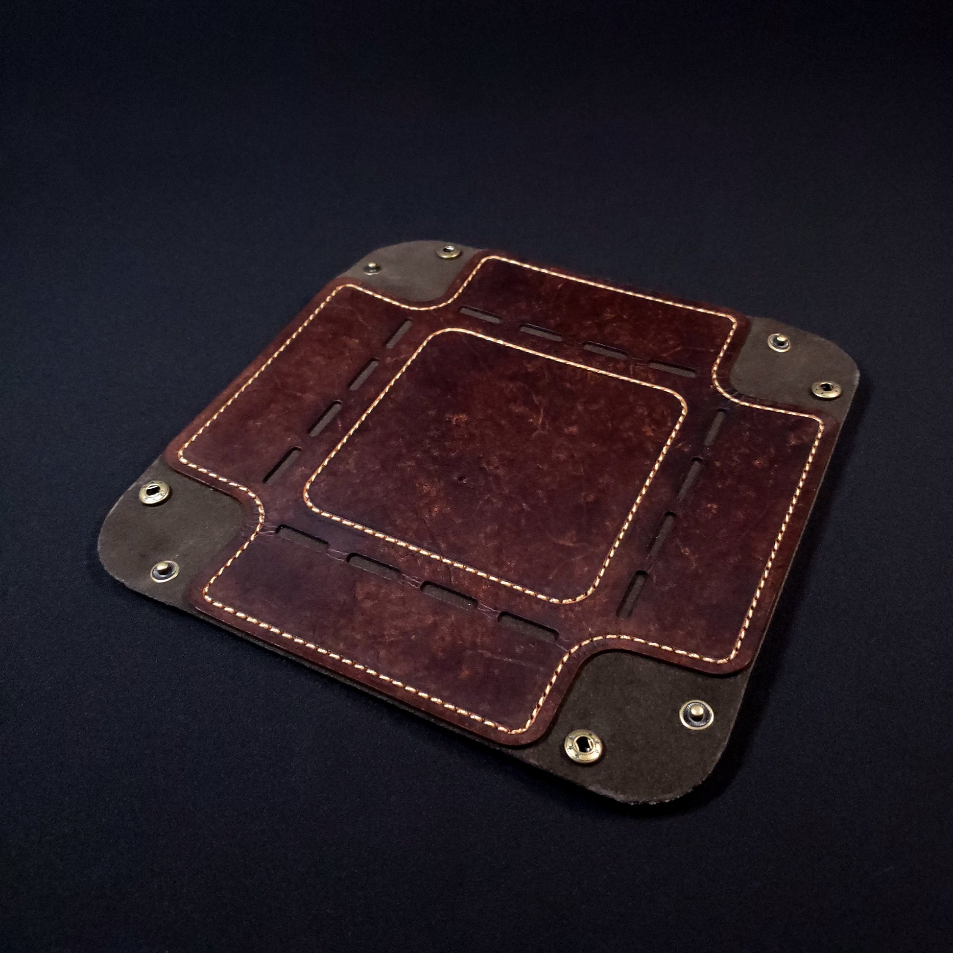 Brown leather dice tray with light brown stitching and bronze buttons, opened and laid flat.