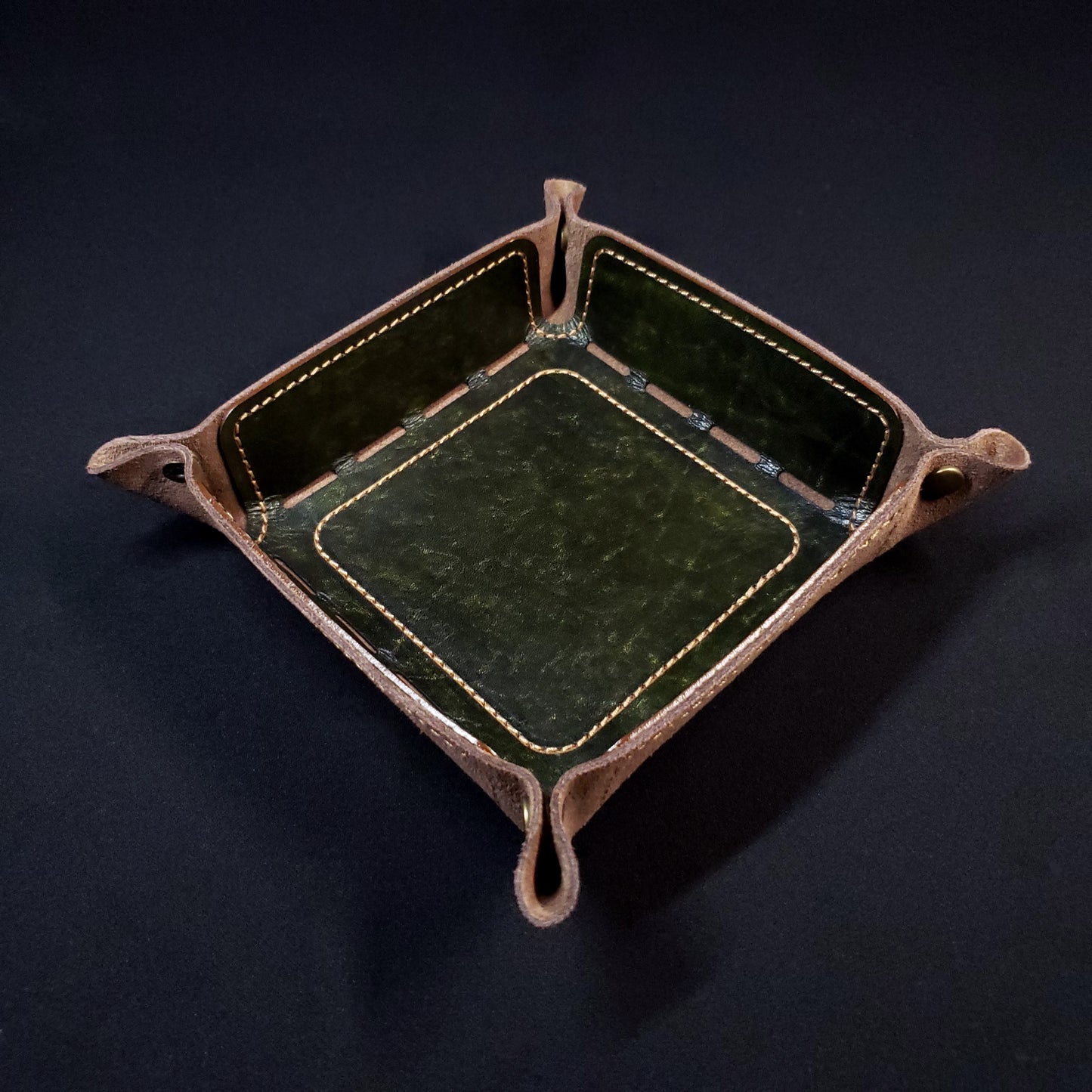 Olive green leather dice tray with light brown stitching and bronze buttons, viewed from the top.
