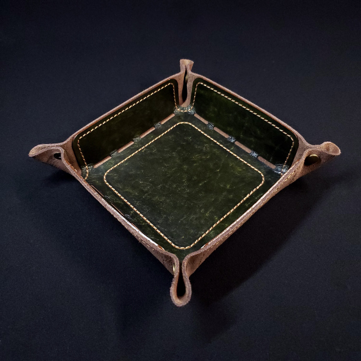 Olive green leather dice tray with light brown stitching and bronze buttons, viewed from the top.