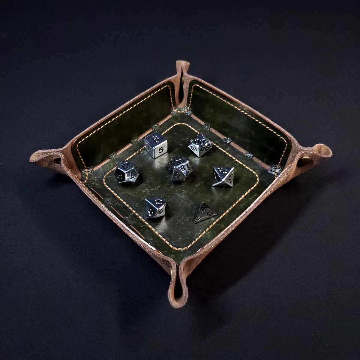 Olive green leather dice tray with brown stitching and bronze buttons with seven dice inside it.