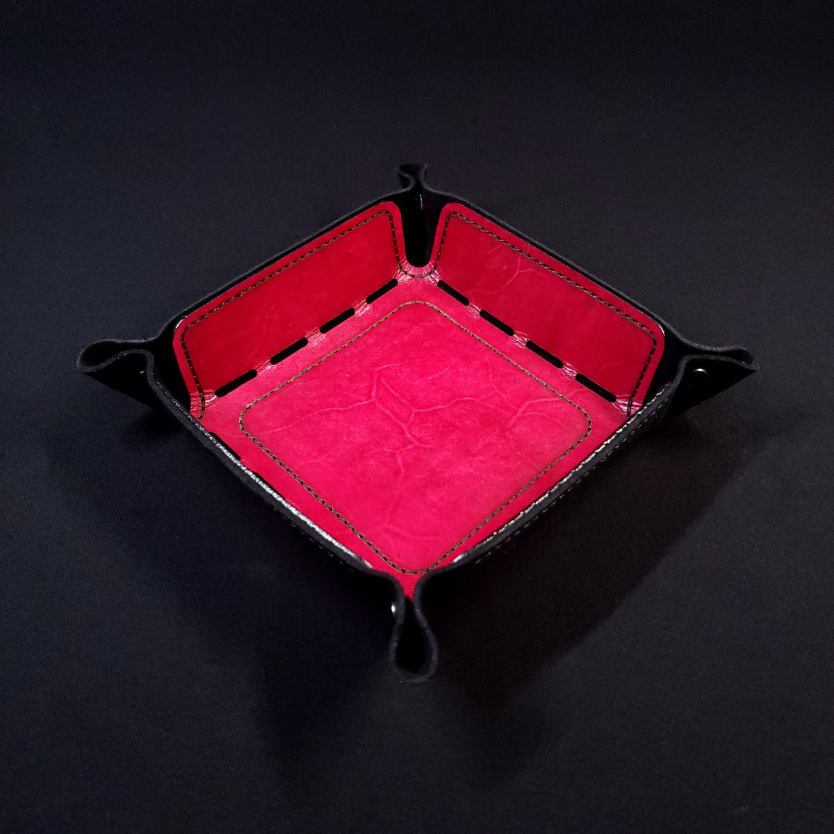 Red leather dice tray with black stitching and gun metal buttons, viewed from the top.