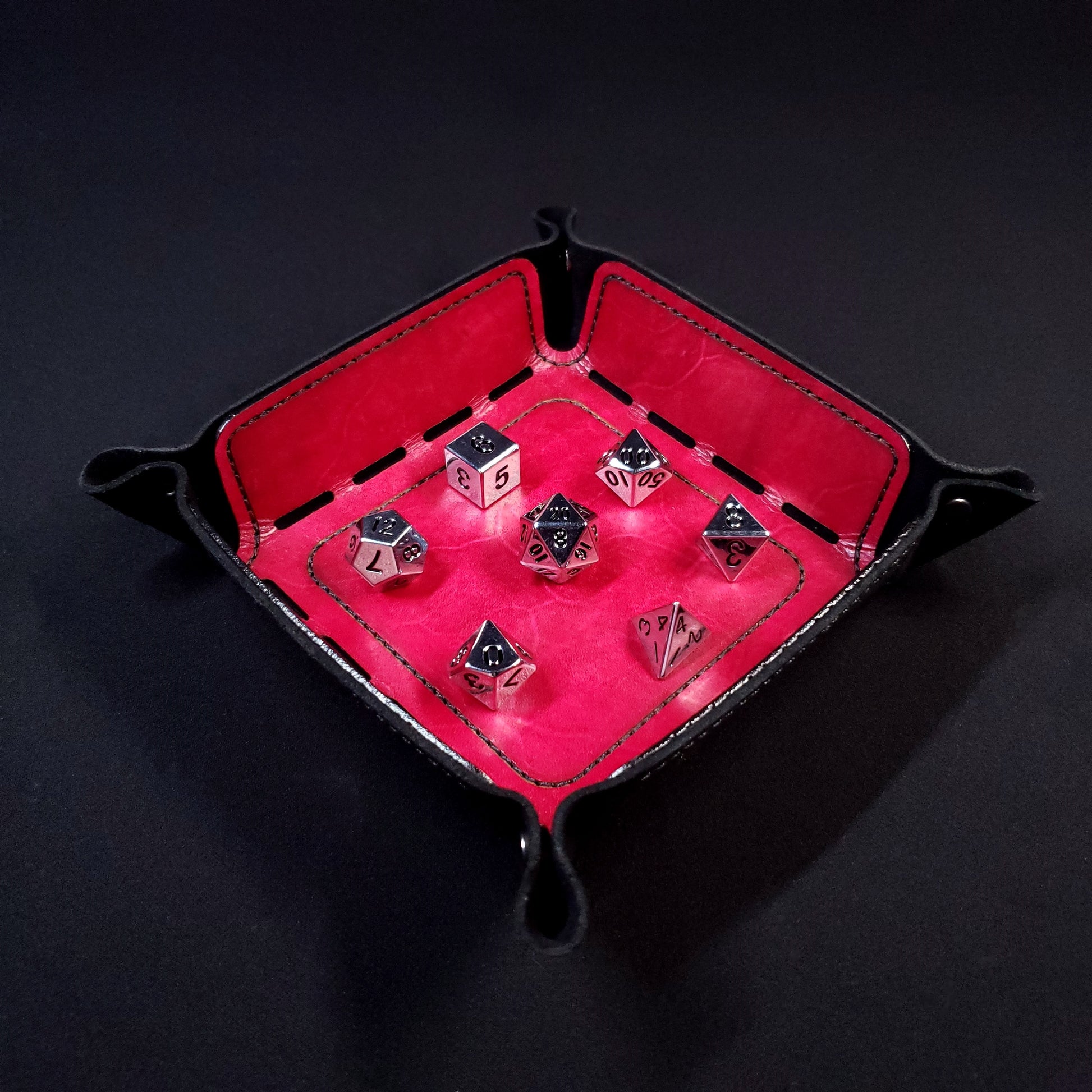 Red leather dice tray with black stitching and gun metal buttons with seven dice inside it.