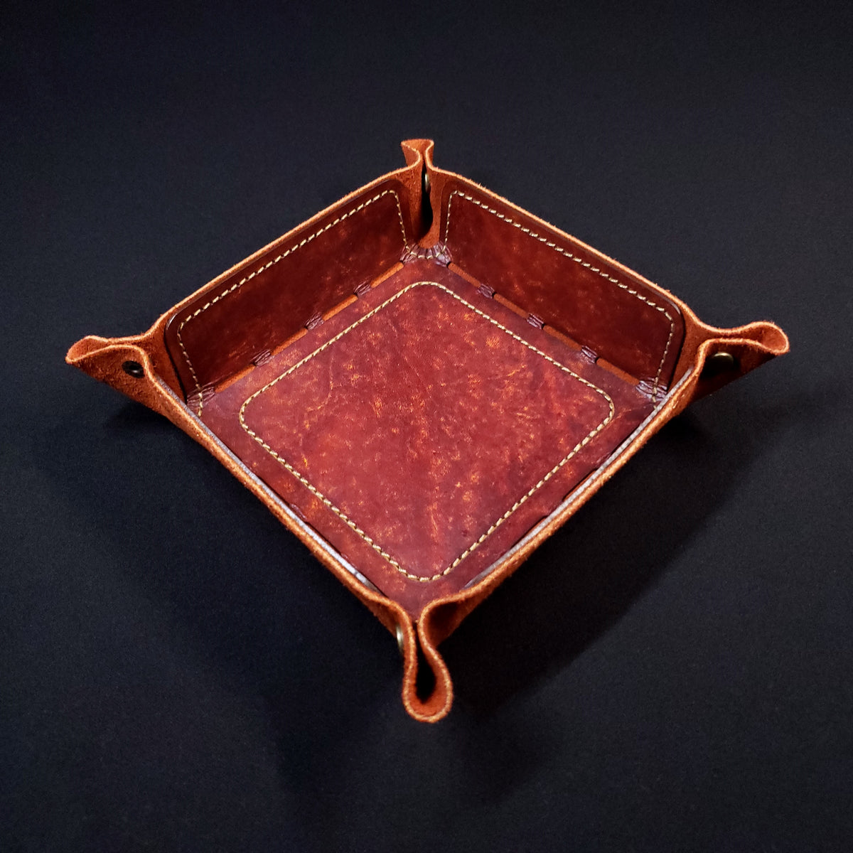 Rust brown leather dice tray with brown stitching and bronze buttons, viewed from the top.