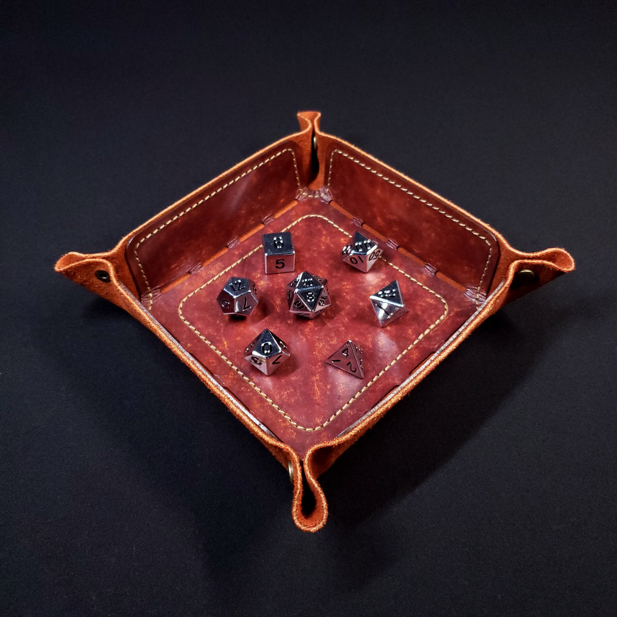 Rust brown leather dice tray with brown stitching and bronze buttons with seven dice inside it.