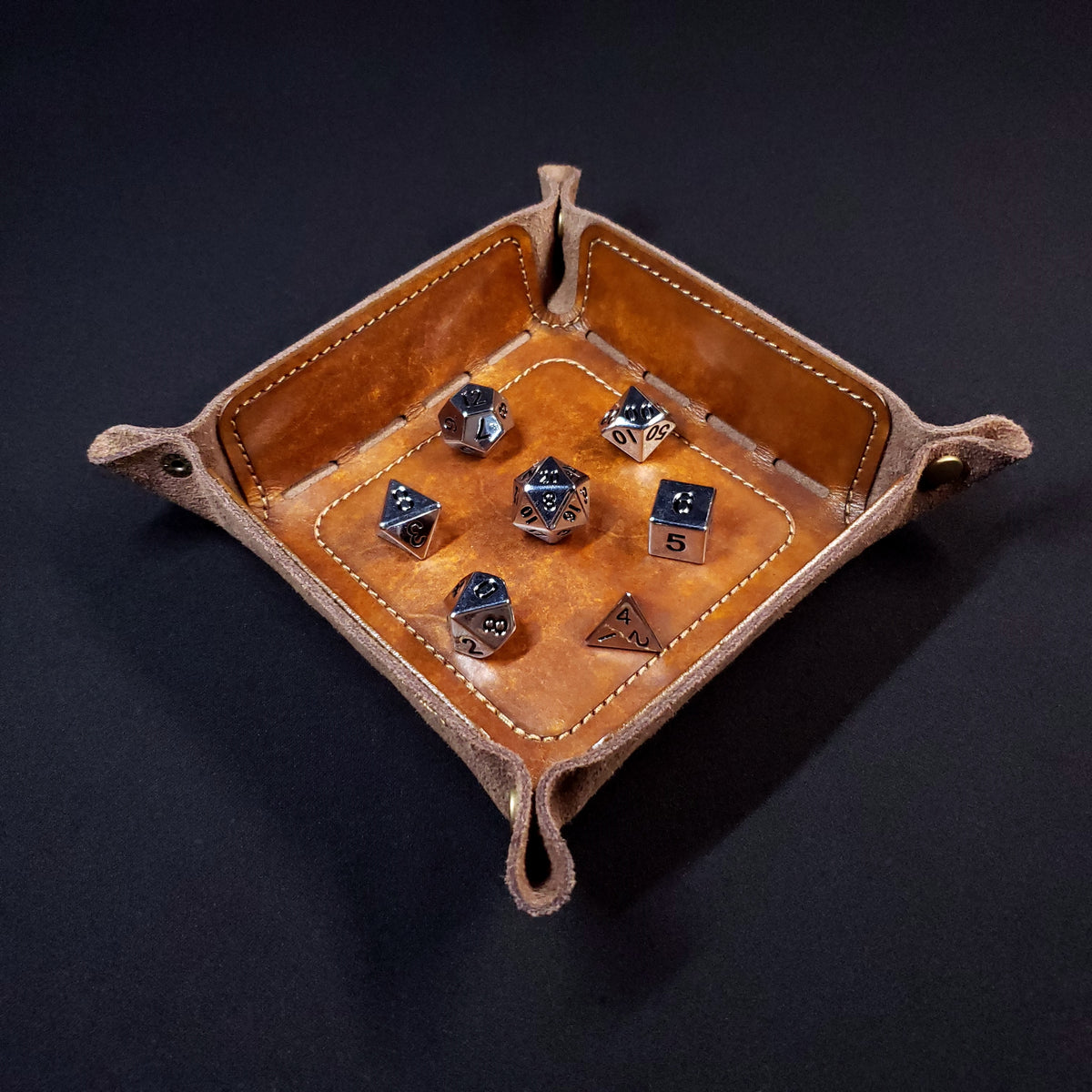 Walnut brown leather dice tray with light brown stitching and bronze buttons with seven dice inside it.